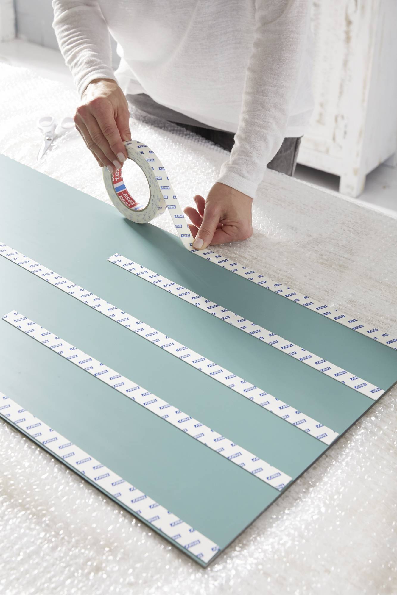 A person is applying double-sided adhesive tape to a large, flat, green board, presumably for securing purposes.