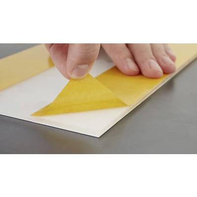 A hand removes yellow protective paper from an adhesive surface on a grey table.
