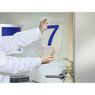 A person in a white coat is sticking a transparent film with the number '7' onto a glass door. Office furniture is visible in the background.