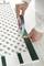 A person is sticking green insulating tape onto a white, braided wooden frame. Hands in close-up, focused work.