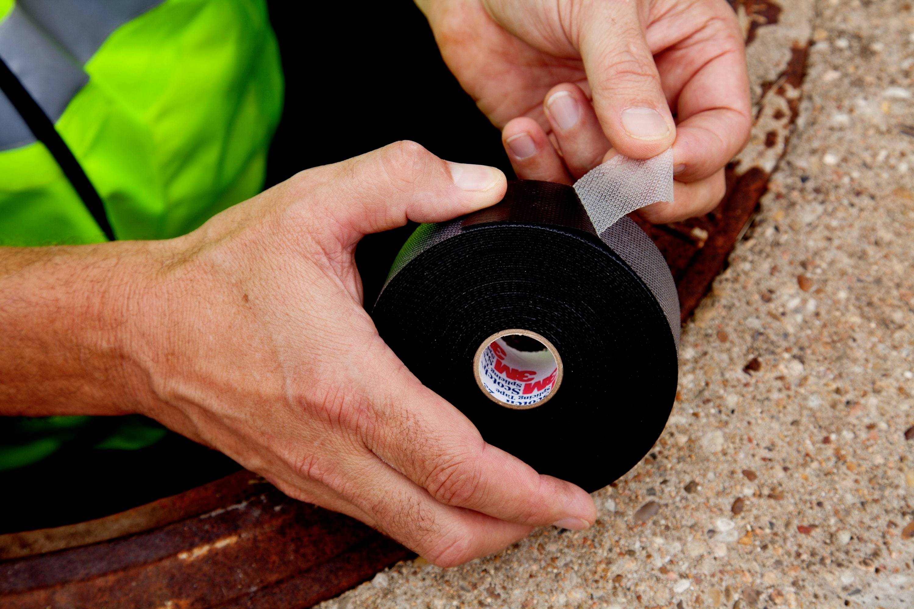 A person is holding a roll of black electrical tape near an open manhole cover. Safety precautions are being prepared.