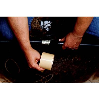 A man is repairing a water pipe outdoors using adhesive tape. Hands are holding the pipe and tape; ground moisture is visible in the background.