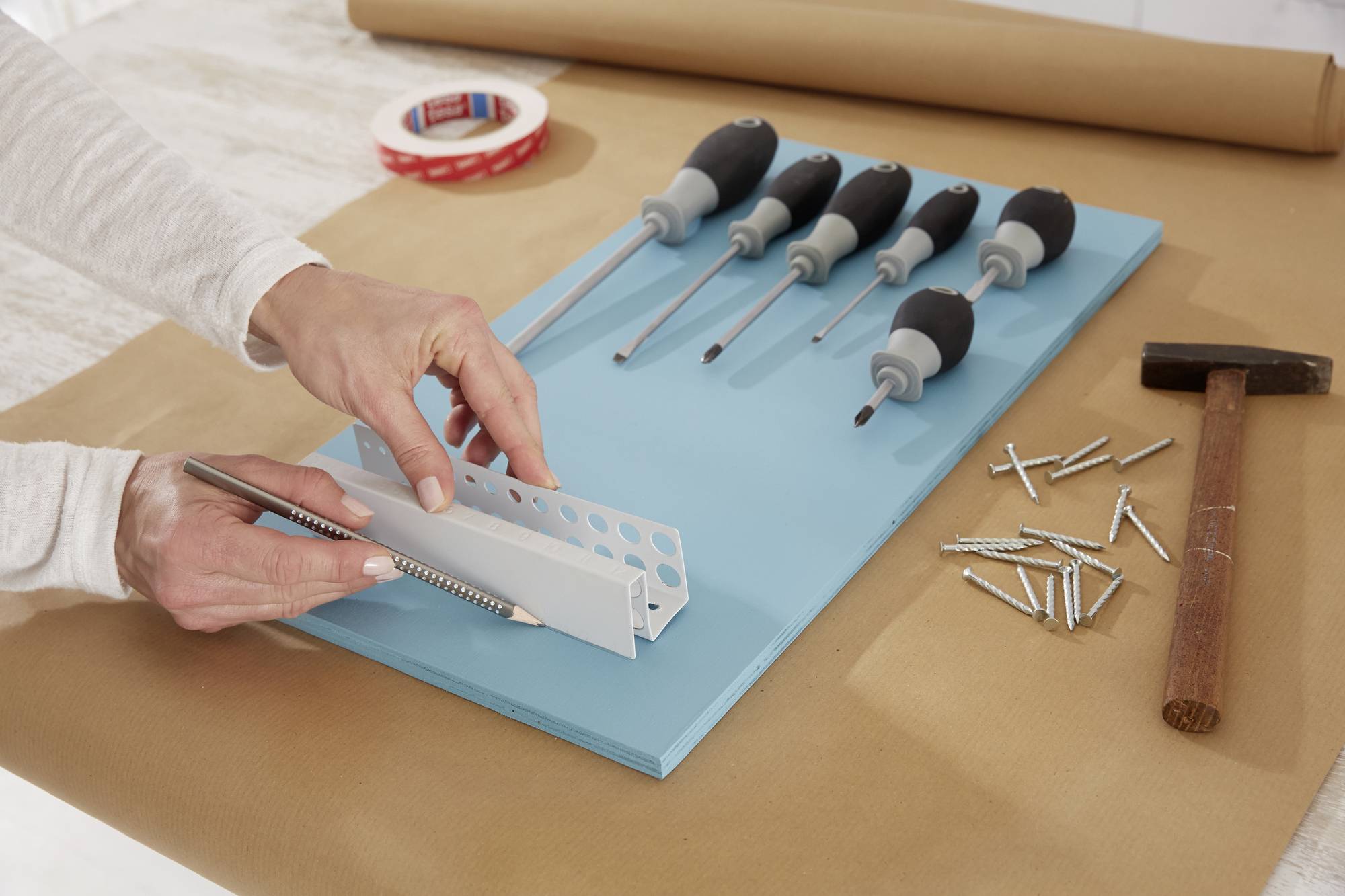 A person is mounting a white metal angle bracket onto a blue plate, surrounded by screwdrivers, screws, and a hammer.