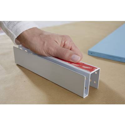A hand is holding a U-shaped metal piece with red adhesive tape, which is lying on a table. Beside it lies a blue rectangle.