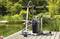 A wet/dry vacuum cleaner with hoses and attachments sits on a wooden deck near a pond surrounded by lush greenery.