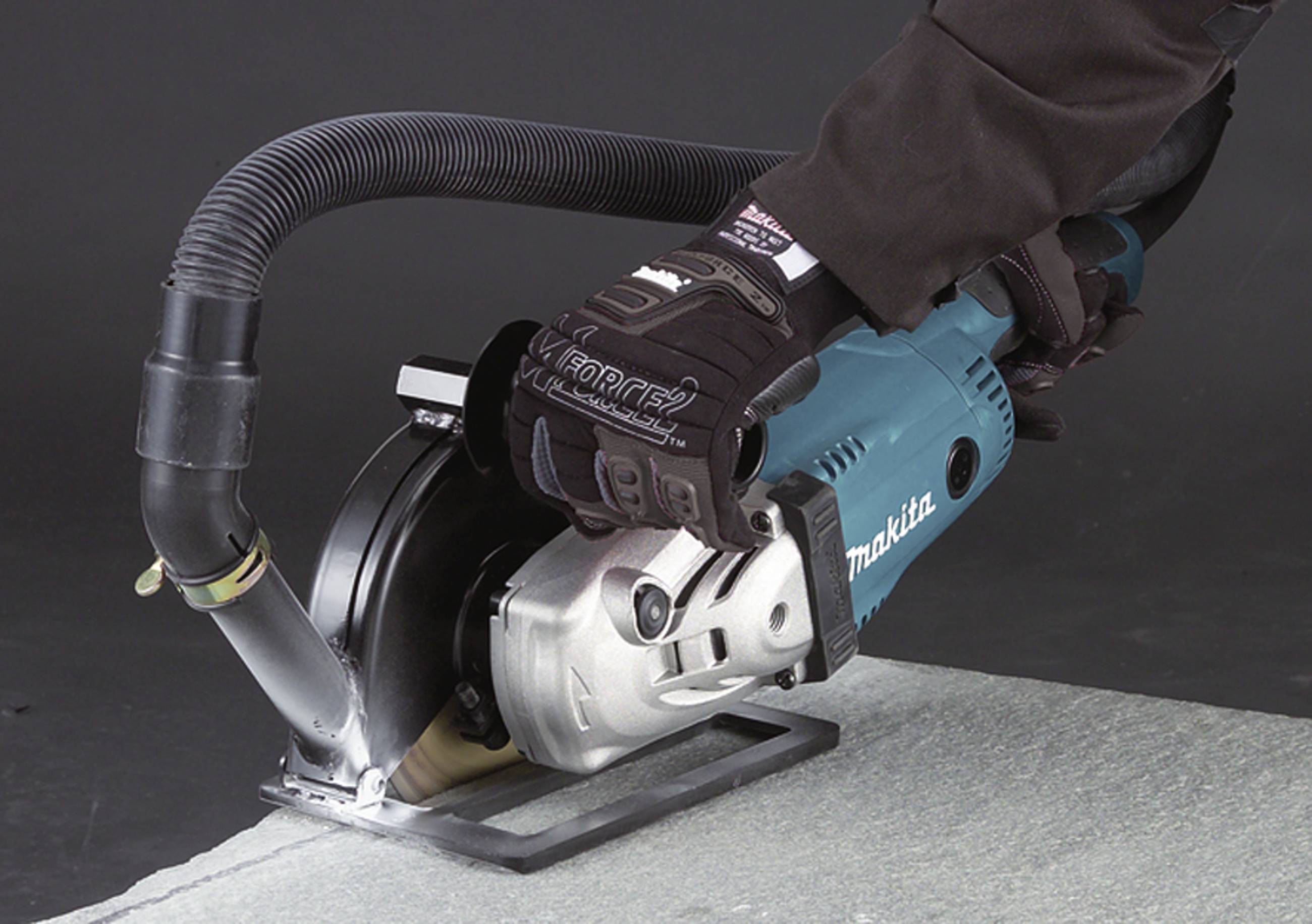 A person is cutting a grey material with a blue electric saw. The saw has dust extraction. Gloves protect the hands.