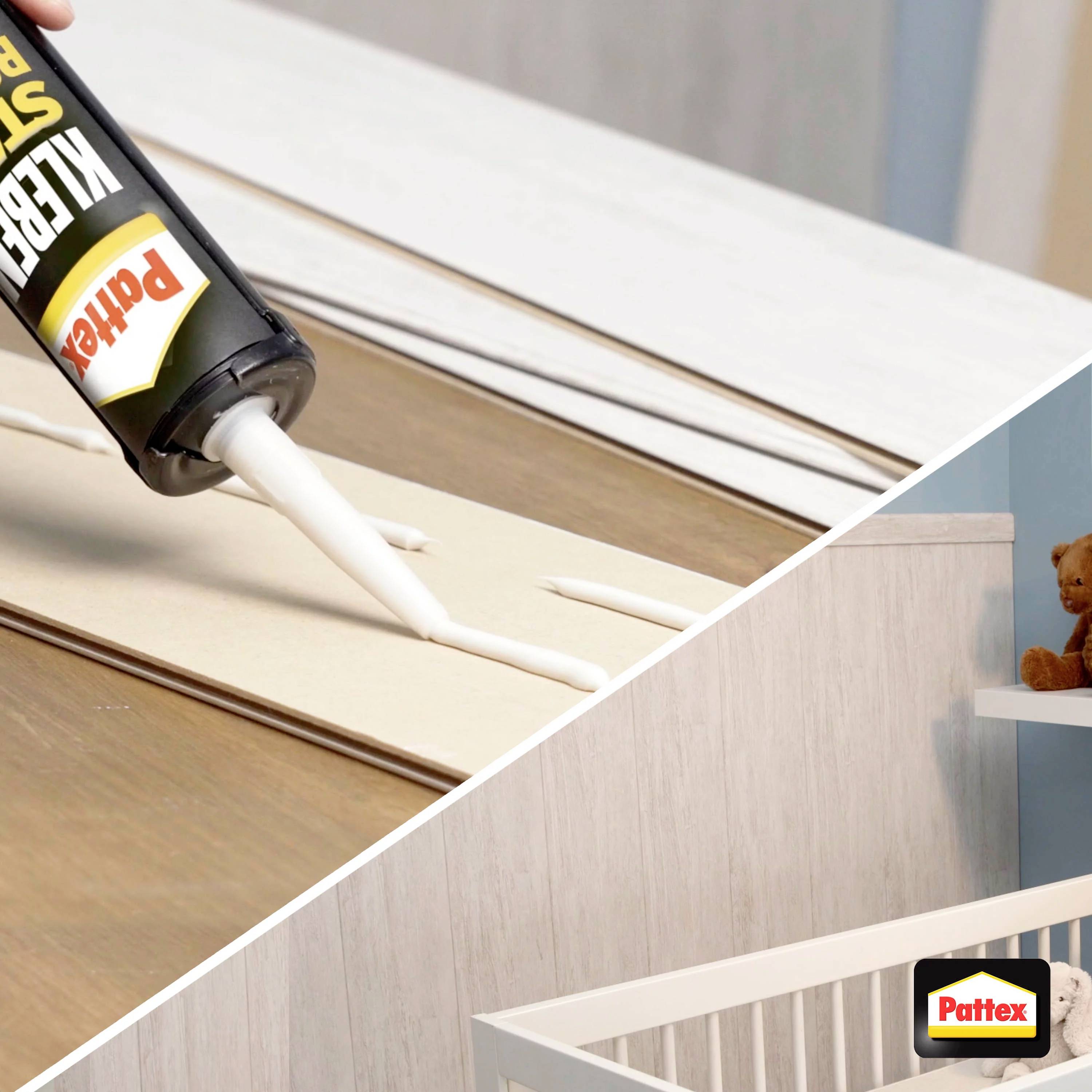 A tube of glue is squeezed over a wooden board. In the background, a children's bedroom with a baby cot and a soft toy can be seen.