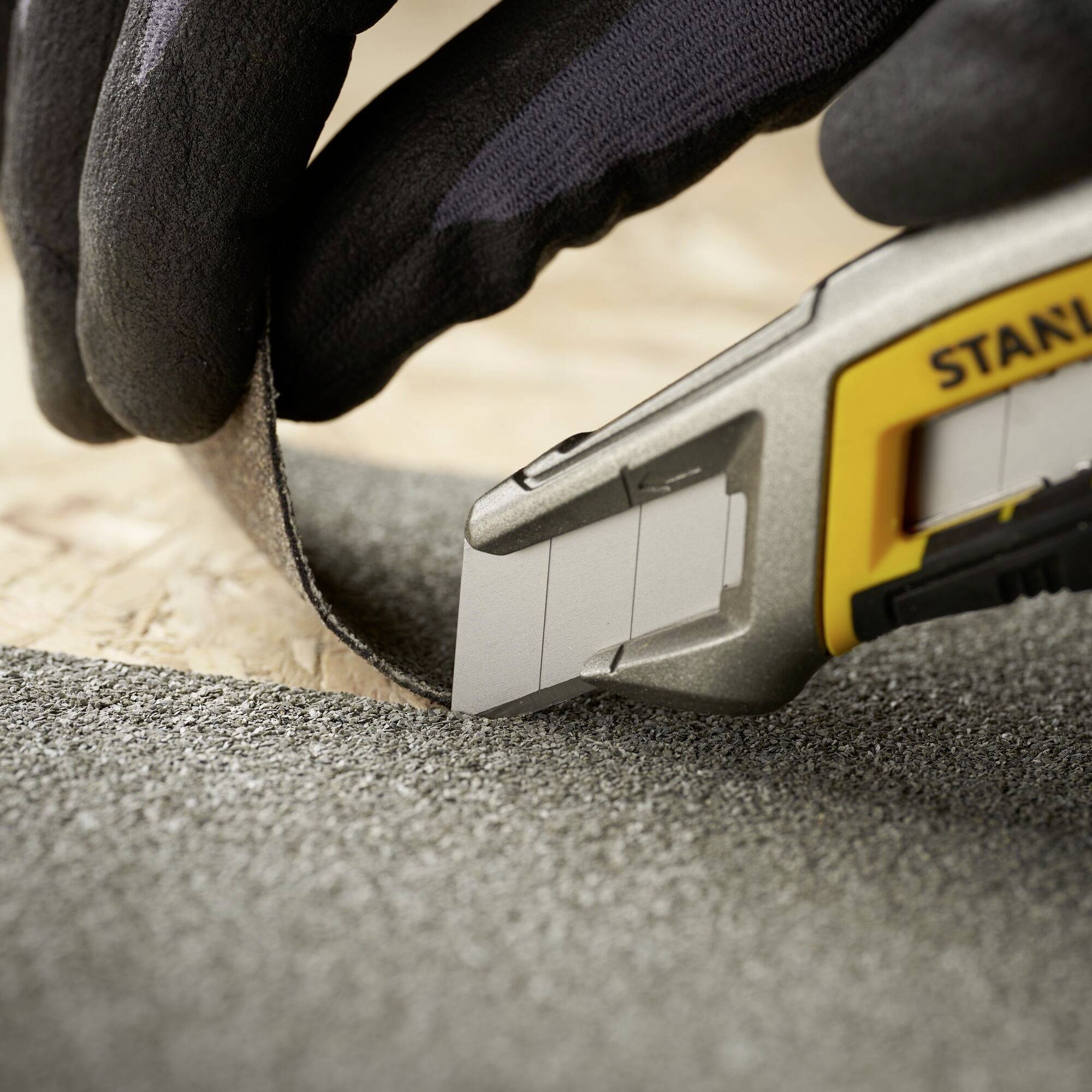 A gloved hand cuts a strip of foam with a utility knife on a wooden surface.