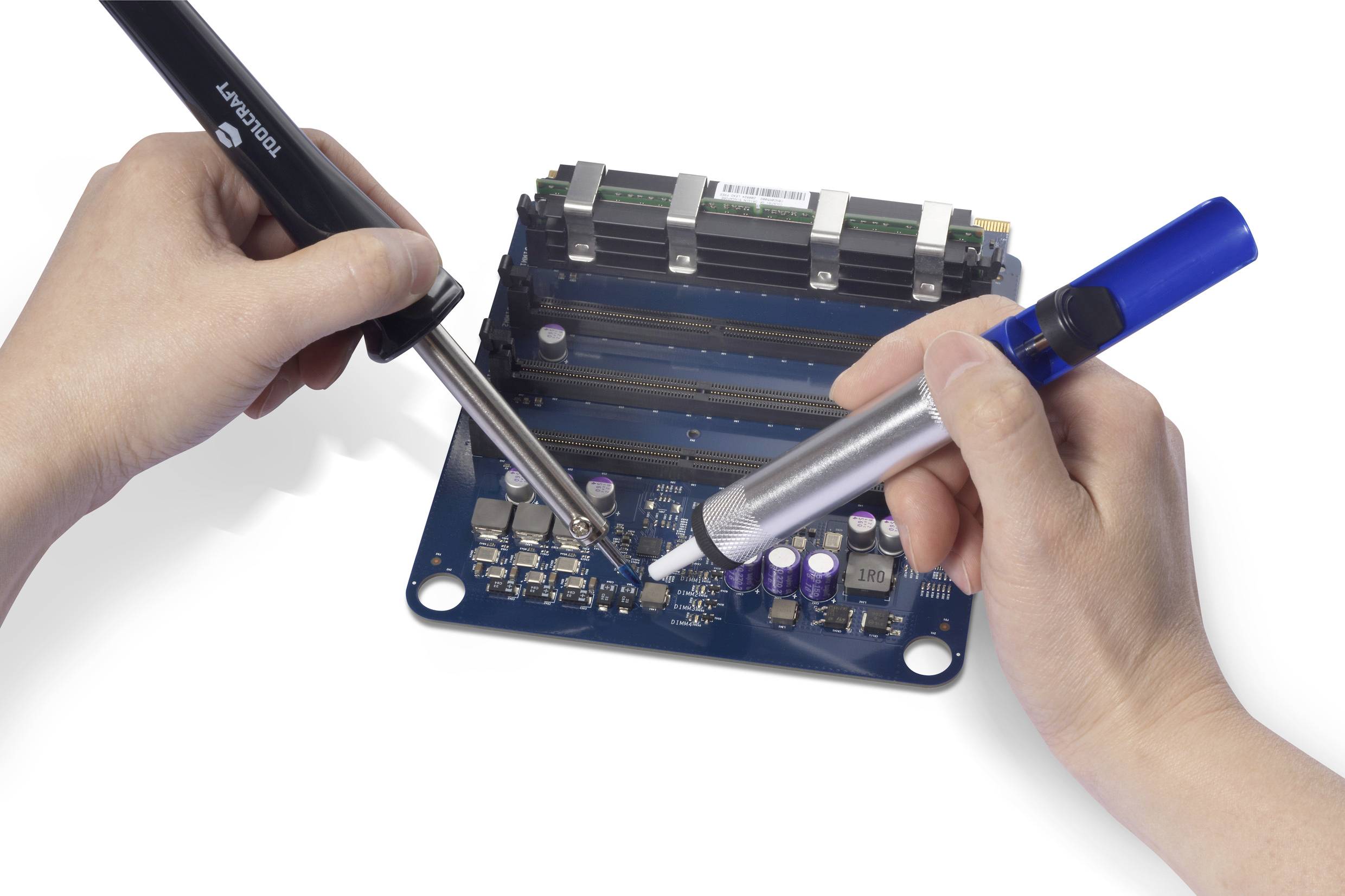 Two hands are working with soldering irons and a desoldering pump on a blue printed circuit board. Various electronic components are visible.
