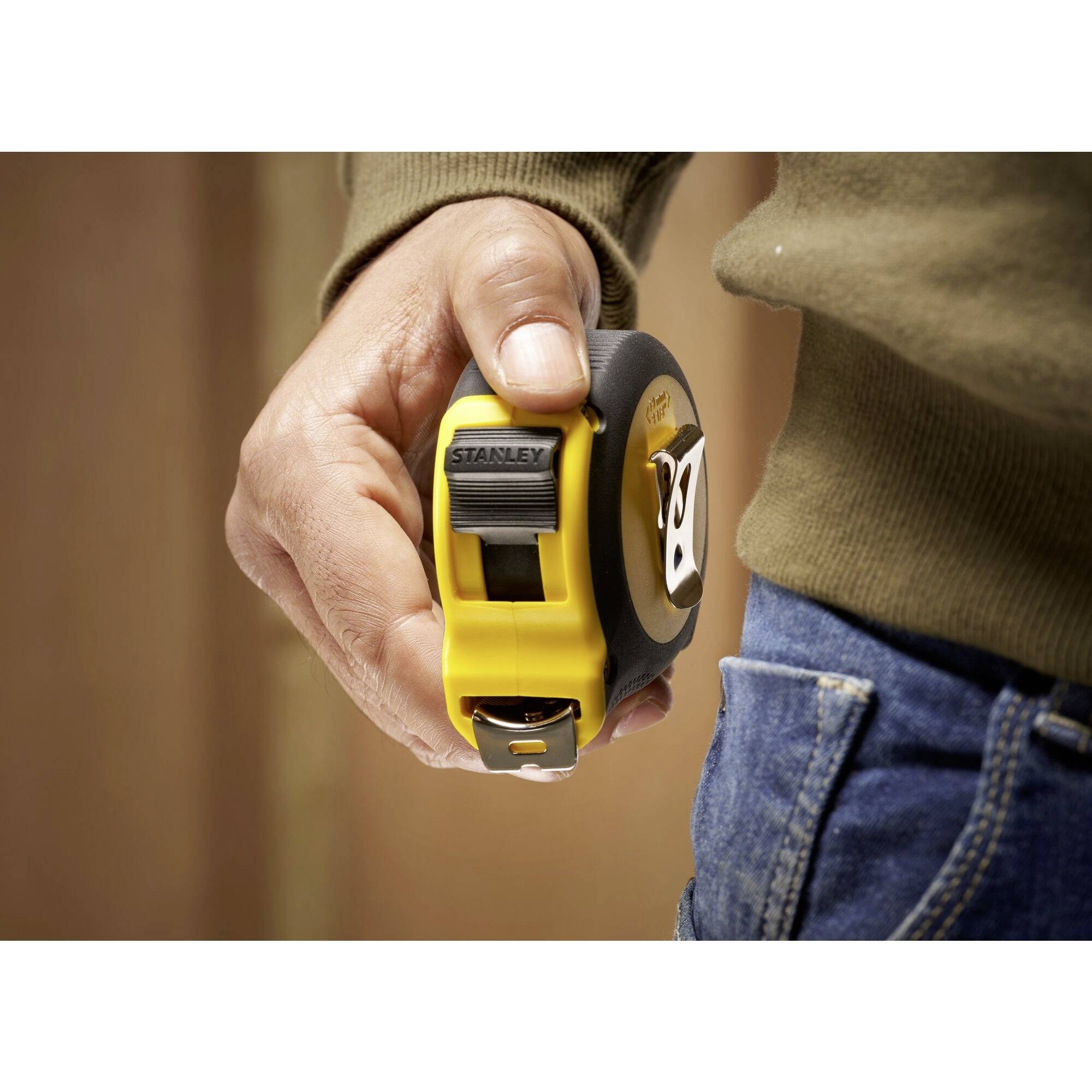 A tape measure is being held in the hand of a person wearing blue jeans.