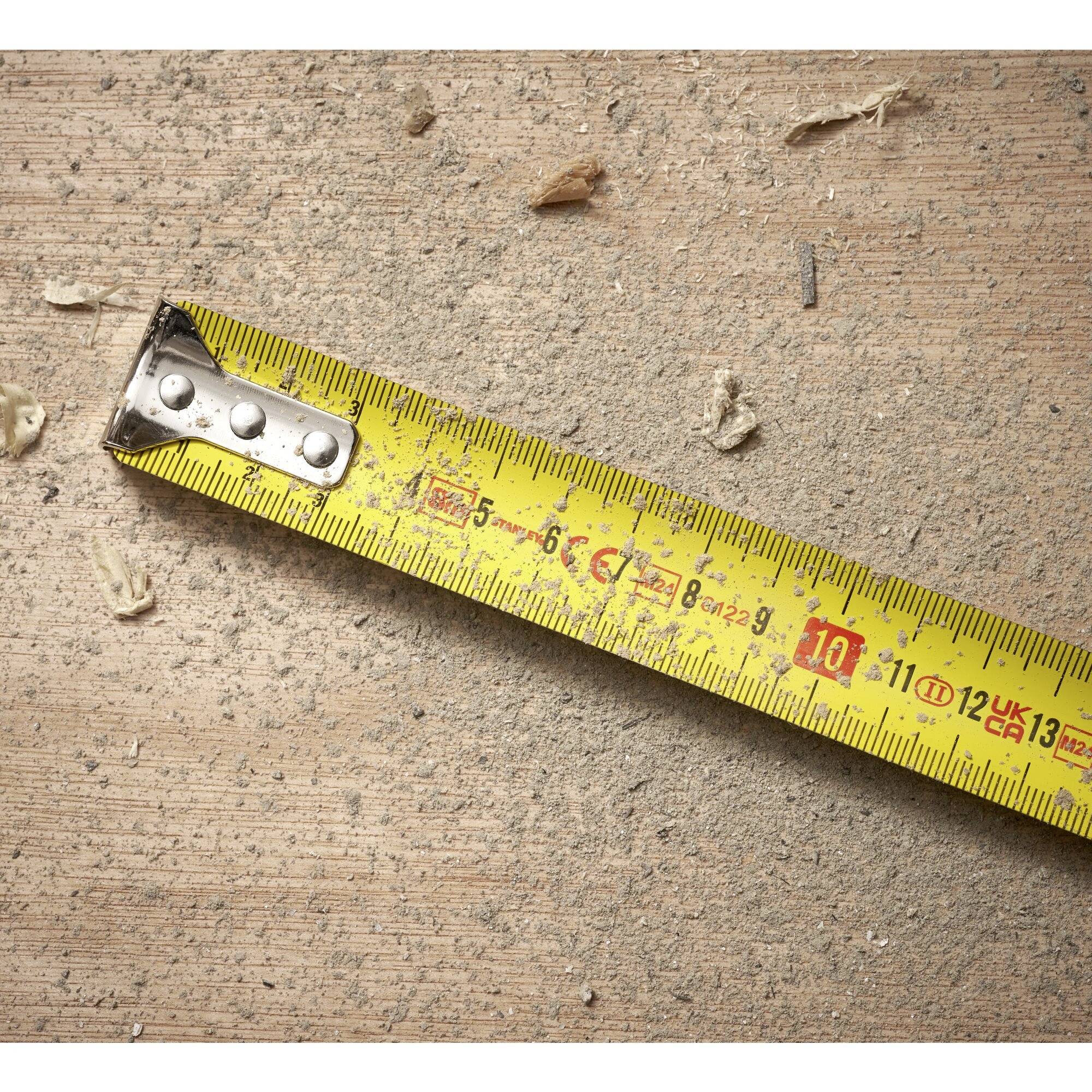 A yellow tape measure lies on a wooden surface with wood shavings and dust.