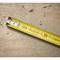 A yellow tape measure lies on a wooden surface with wood shavings and dust.