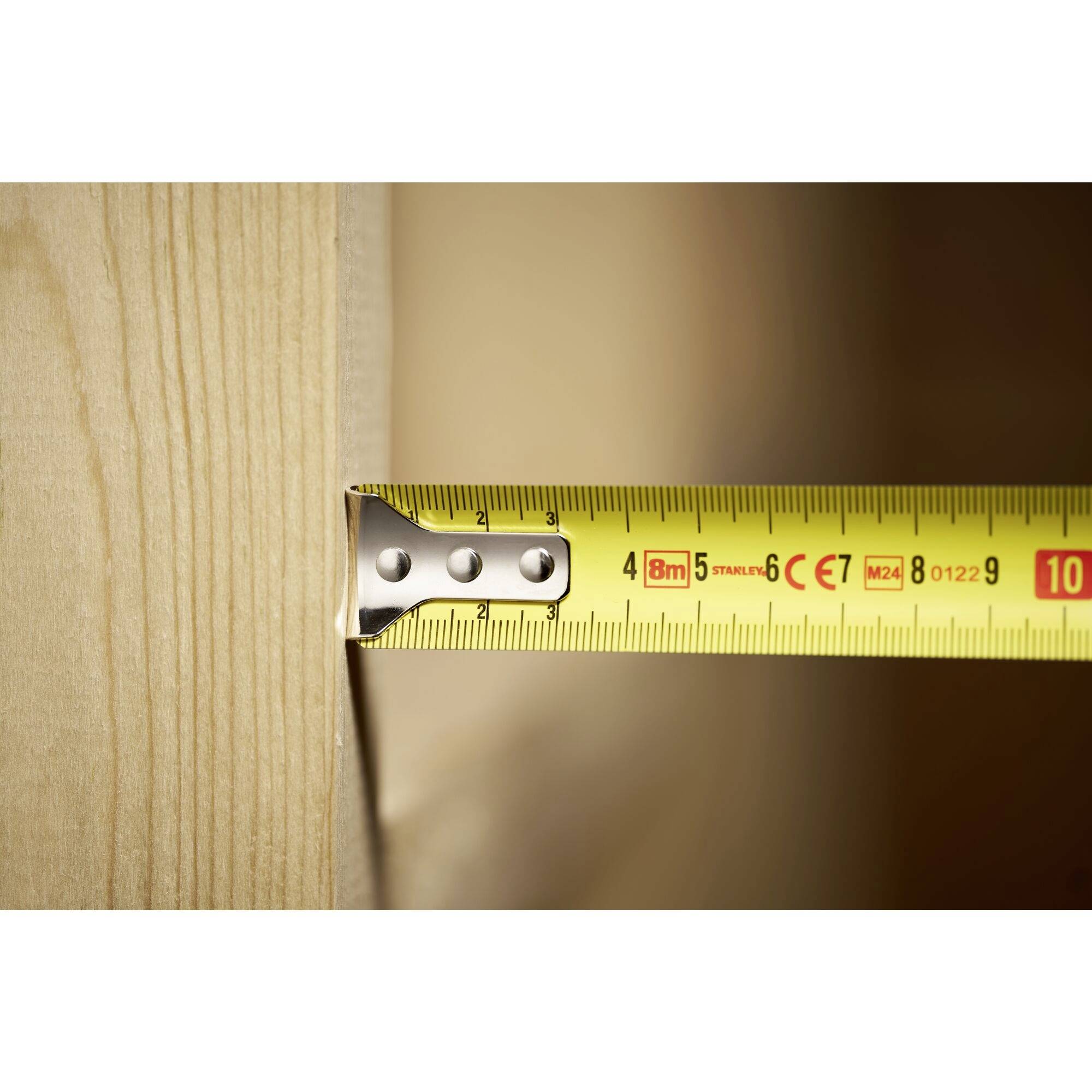 Close-up of a yellow tape measure lying on a wooden beam, showing a length of 9 cm.