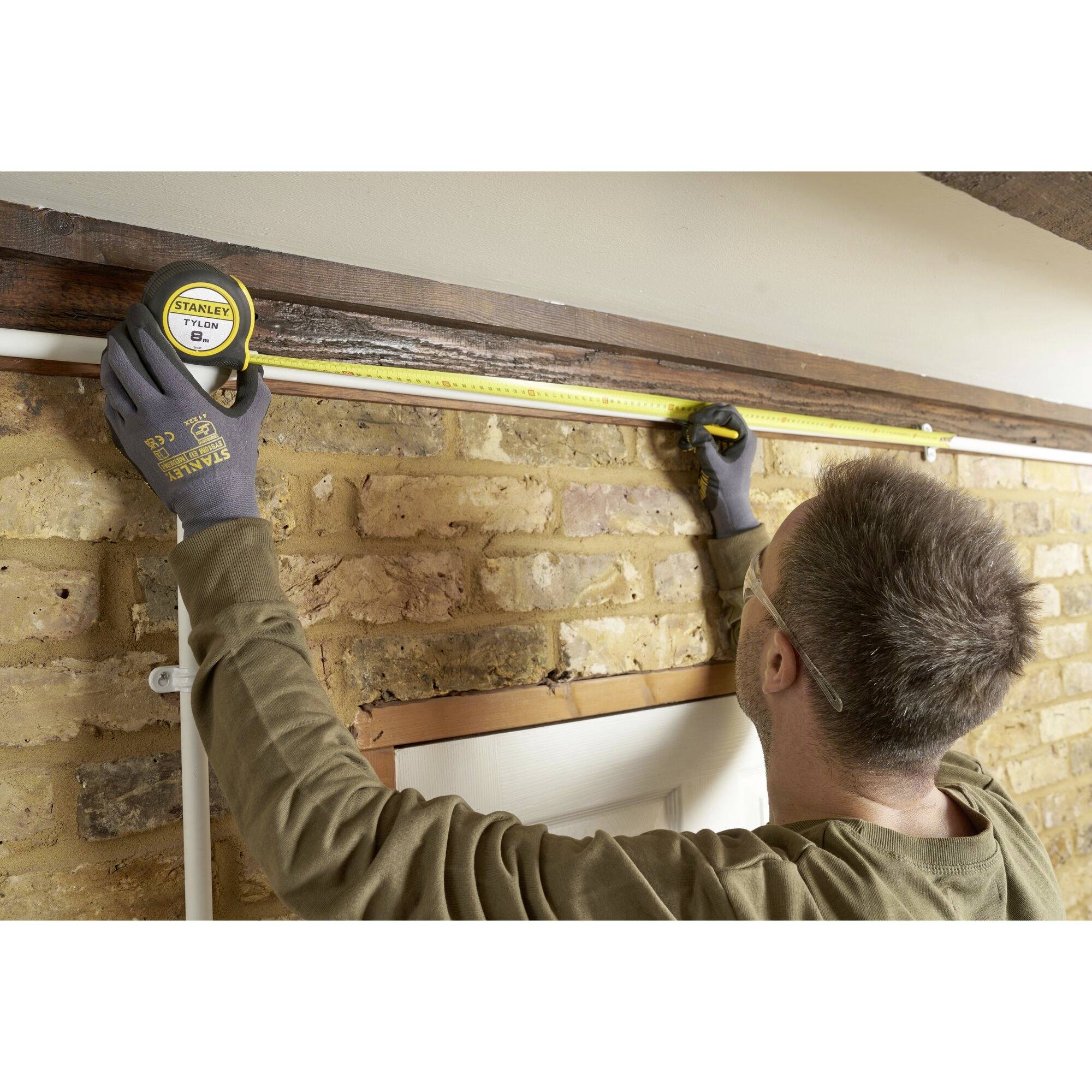 A person is measuring the width of a door frame on a brick wall using a tape measure.