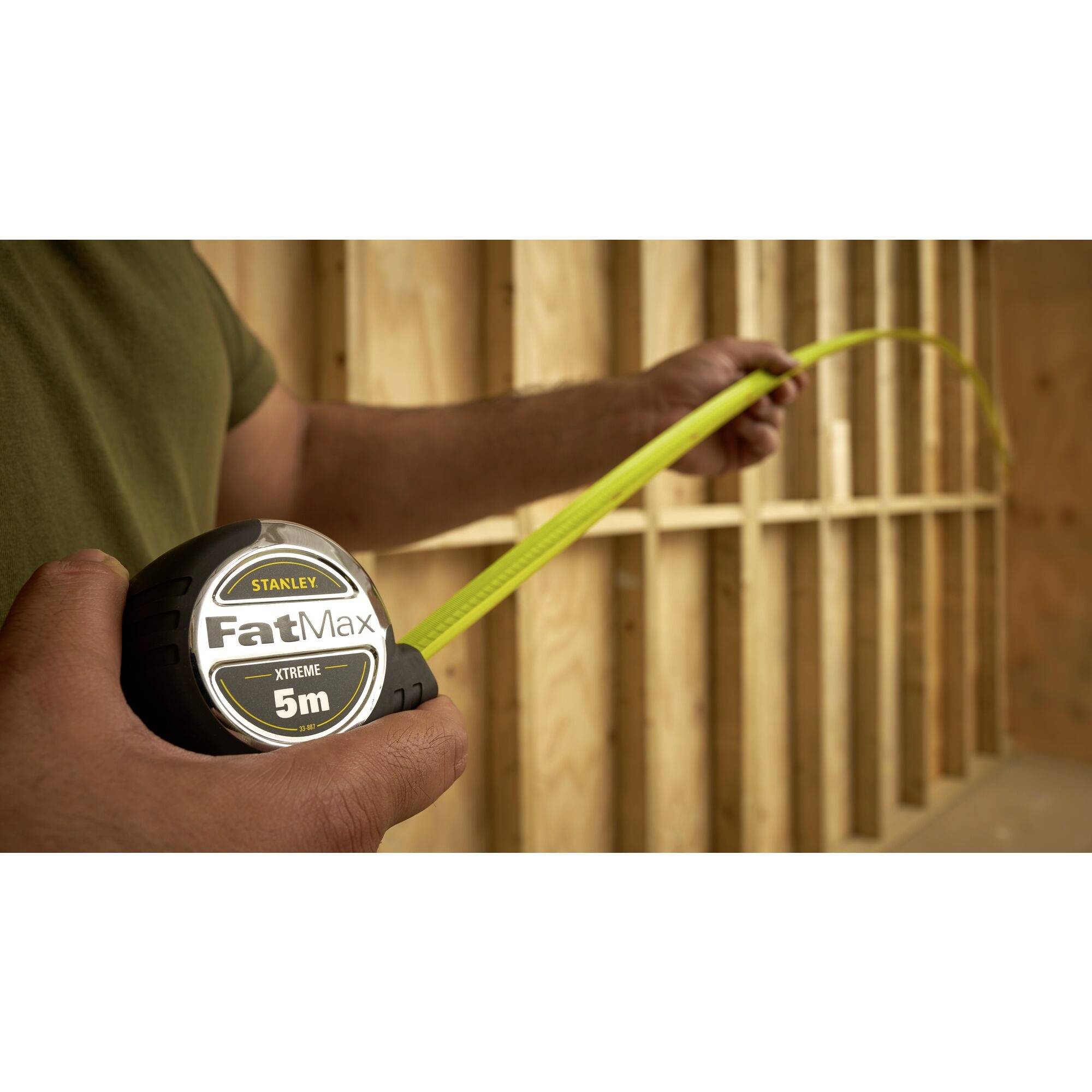 A person is measuring with a yellow tape measure in a timber-framed building. The tape measure reads 'Stanley FatMax 5m'.