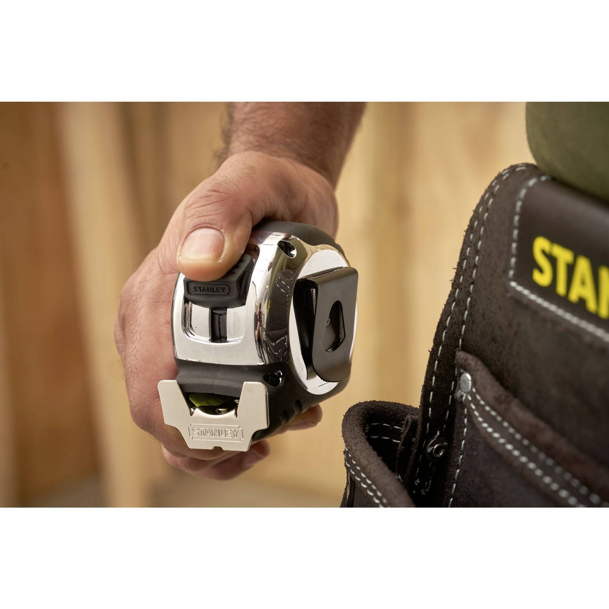 'Hand holding a tape measure.' A construction worker is holding a silver tape measure, ready to measure. A tool bag is visible in the background.