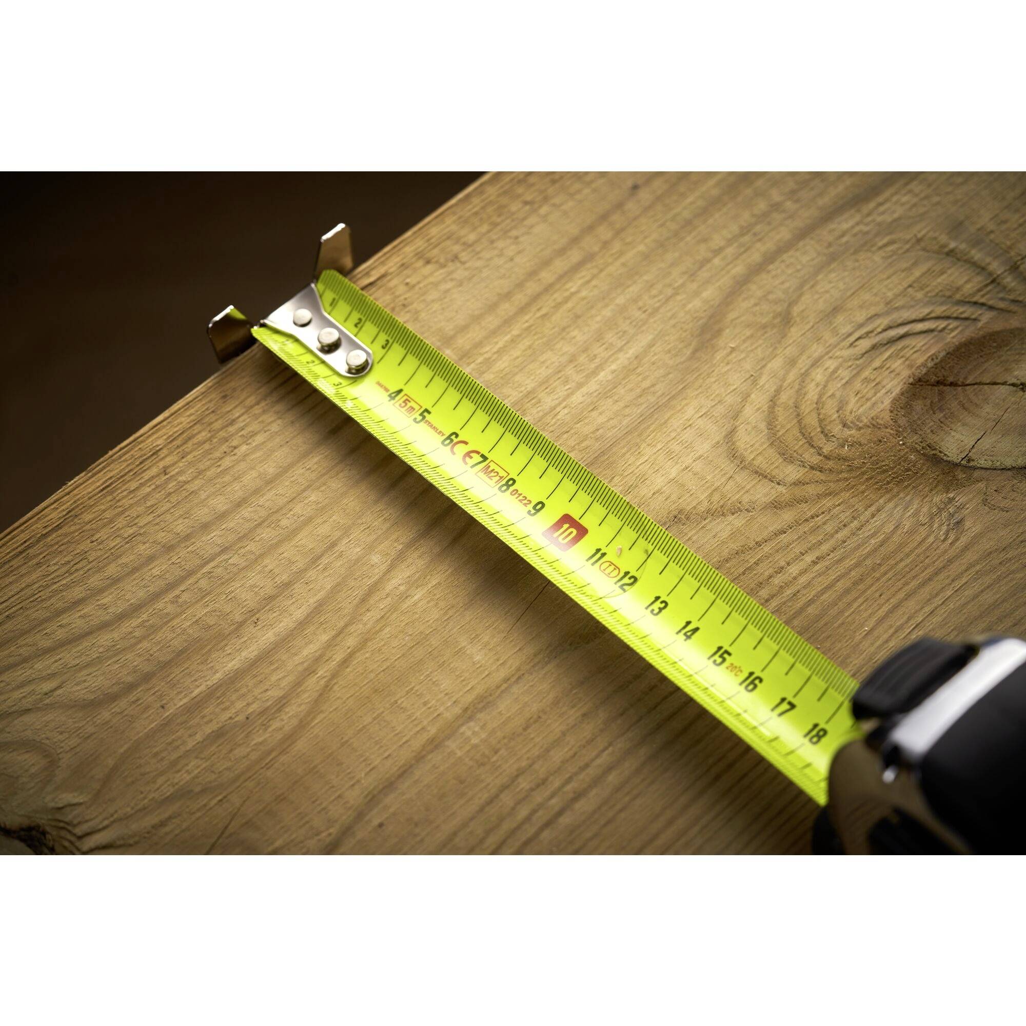 A yellow measuring tape lies on a wooden board and indicates a length of approximately 12.2 cm. The board has a visible wood grain.