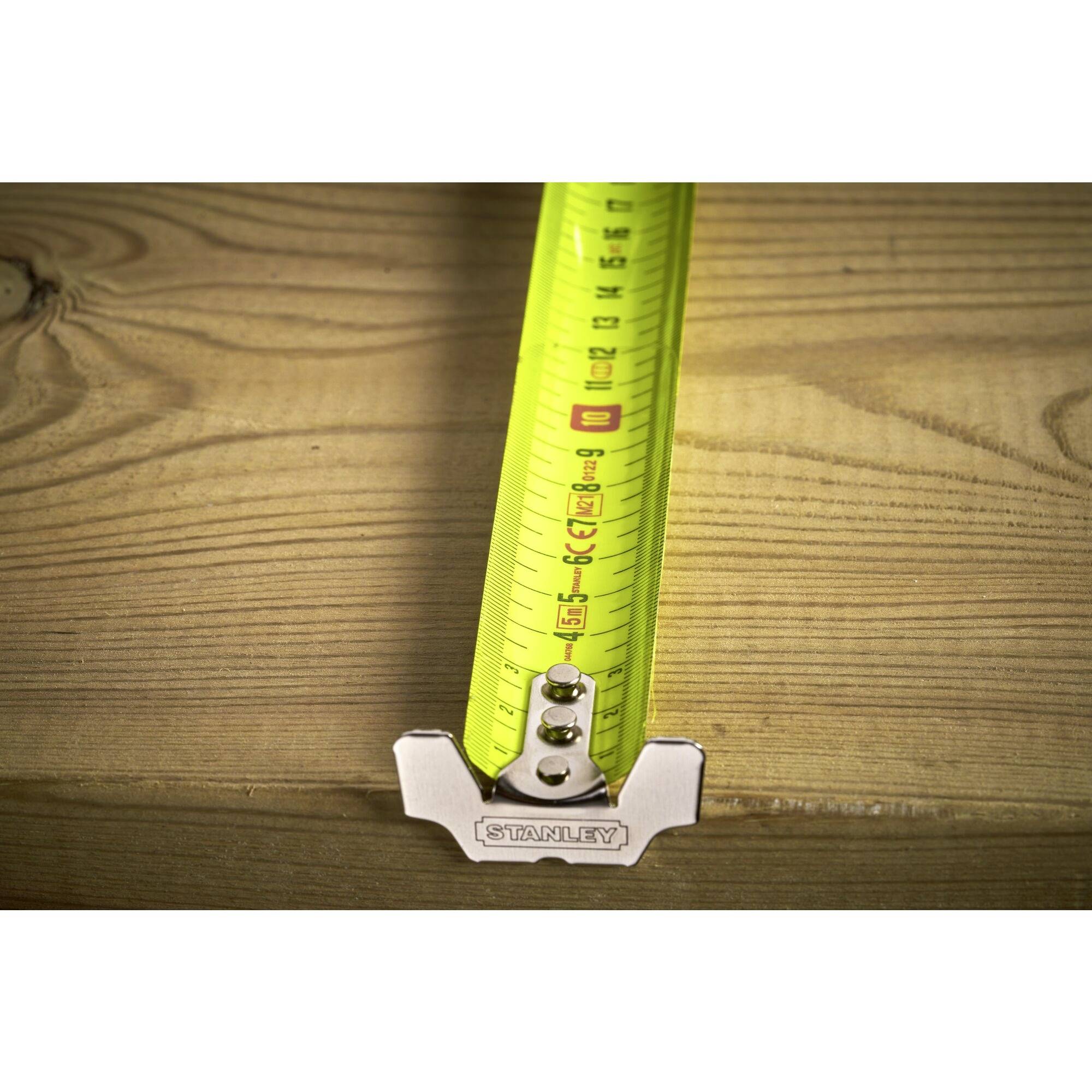 A measuring tape in bright yellow is being measured on a wooden board. It indicates a length of approximately 19 cm.