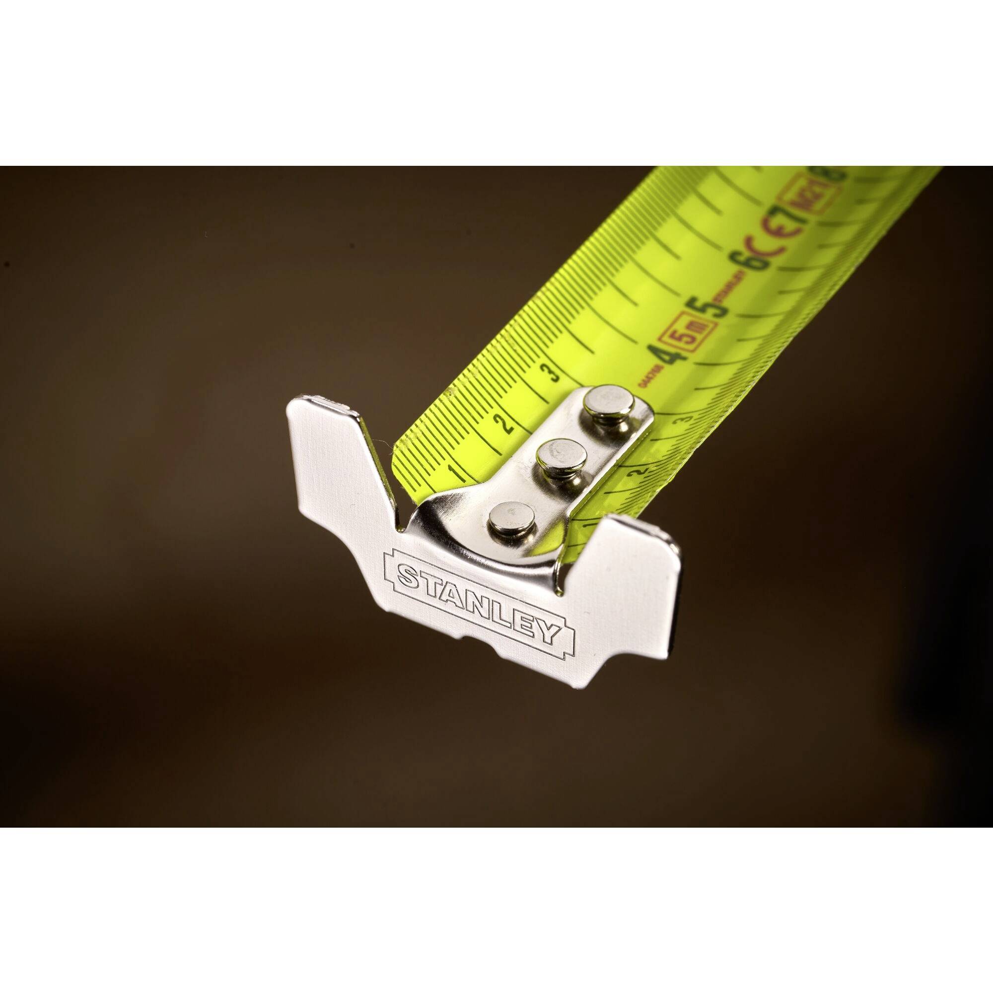 A yellow tape measure with metal hooks that has been unrolled, bearing the 'Stanley' name. The tape shows centimetre and millimetre markings.