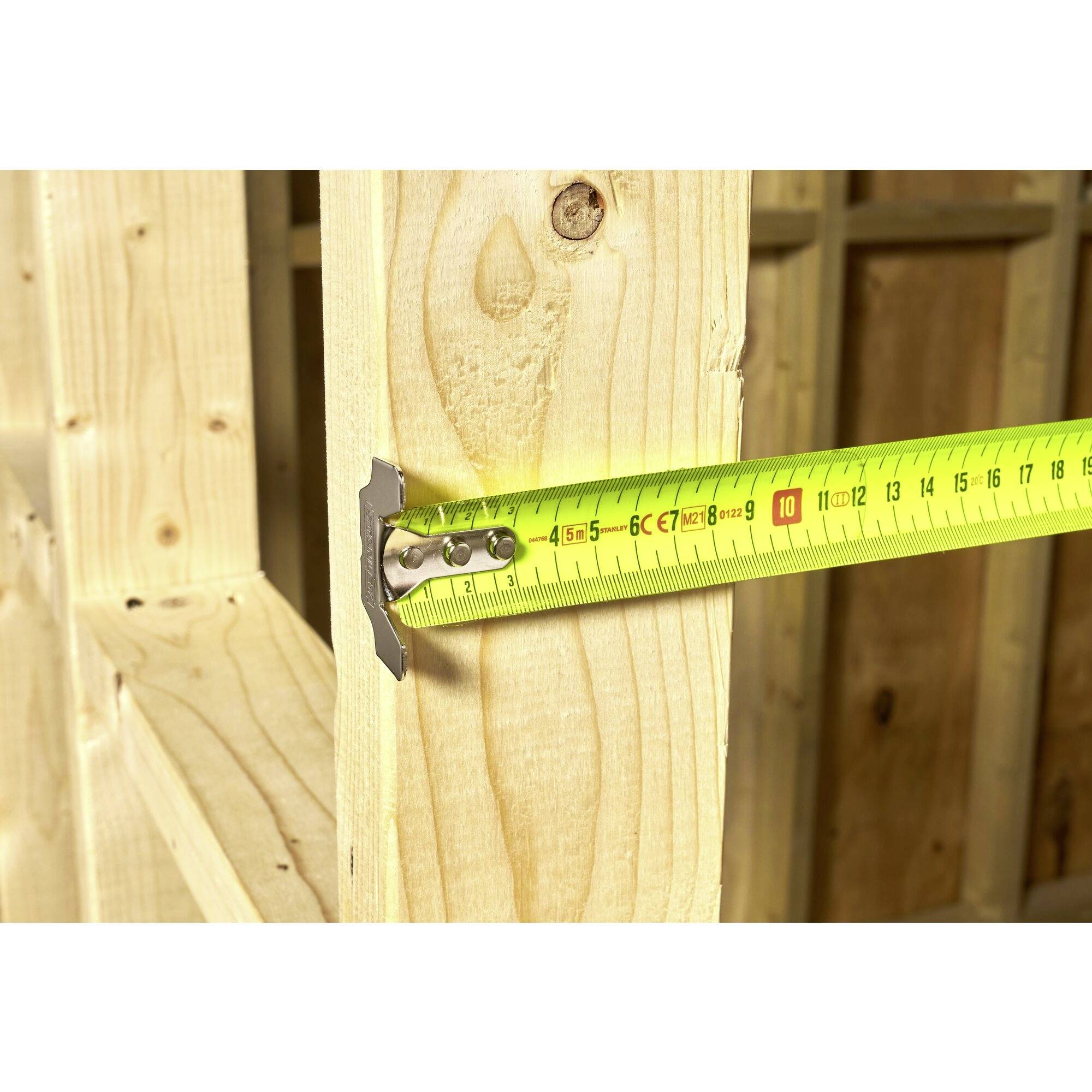 A yellow tape measure is measuring a wooden beam. The length is approximately 10 cm. The wood grain and details of the tape measure are visible.