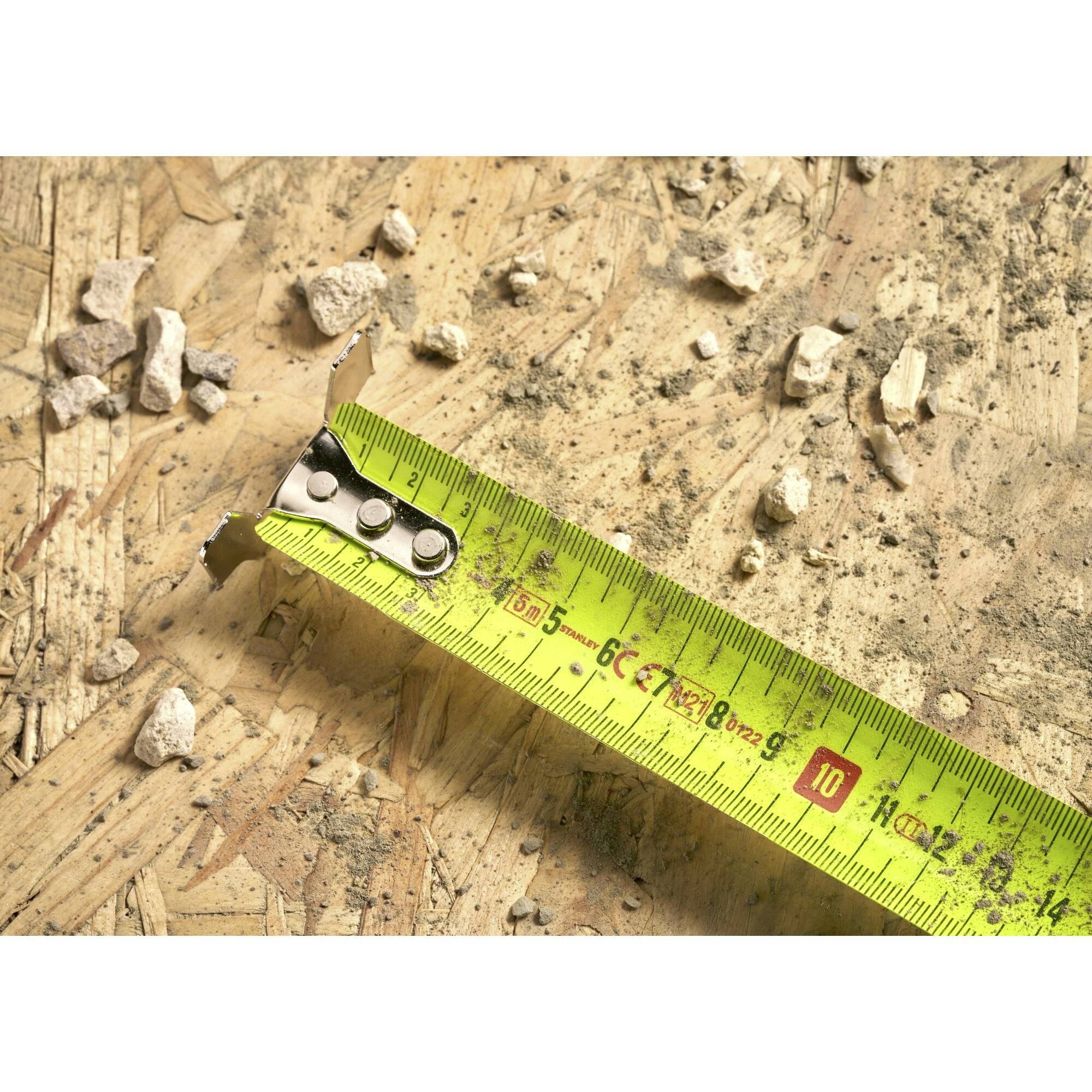 Tape measure lies on plywood with plaster chunks. It shows 10 cm to illustrate construction progress or material measurement.
