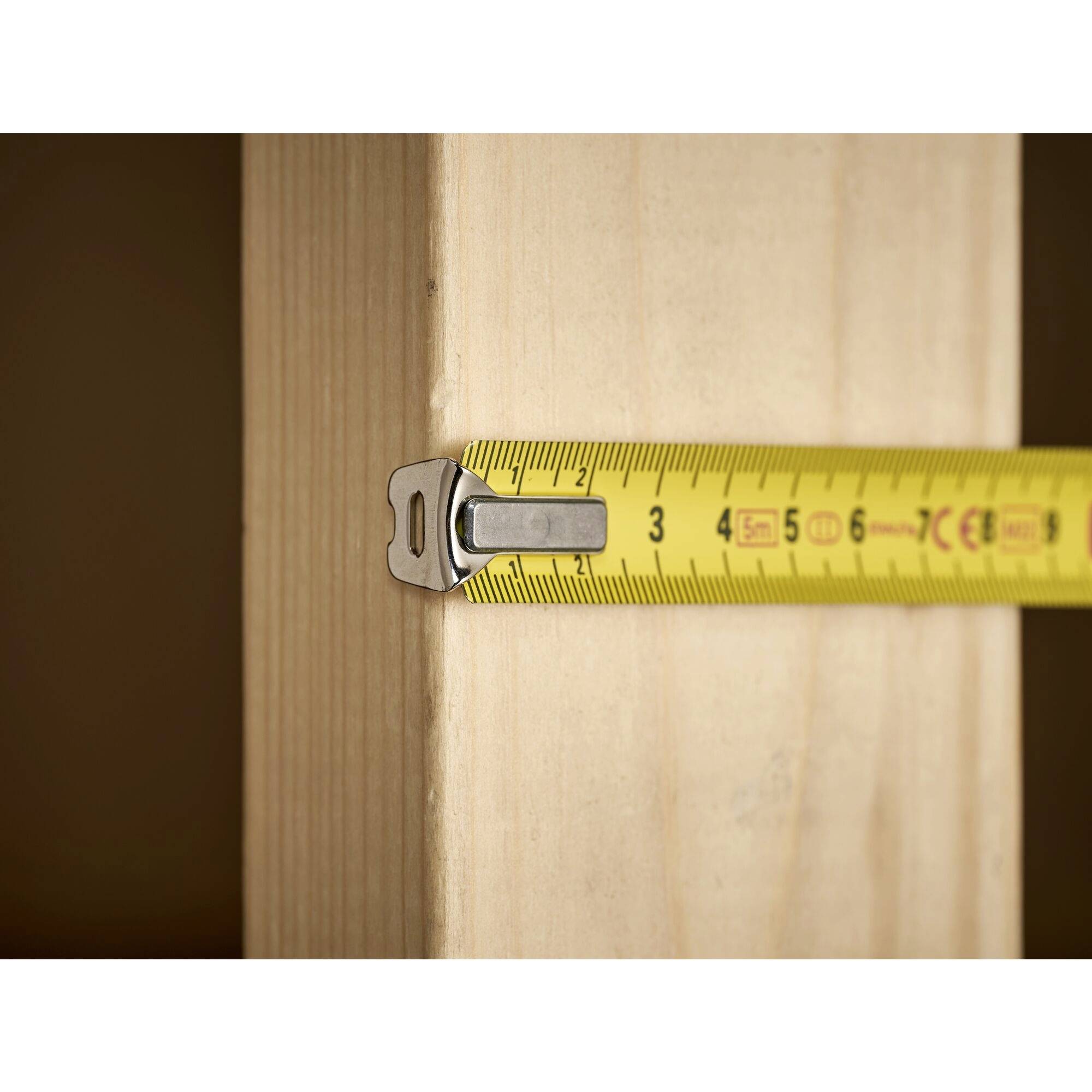 A yellow tape measure is measuring the width of a wooden beam with a reading of approximately 3 cm.