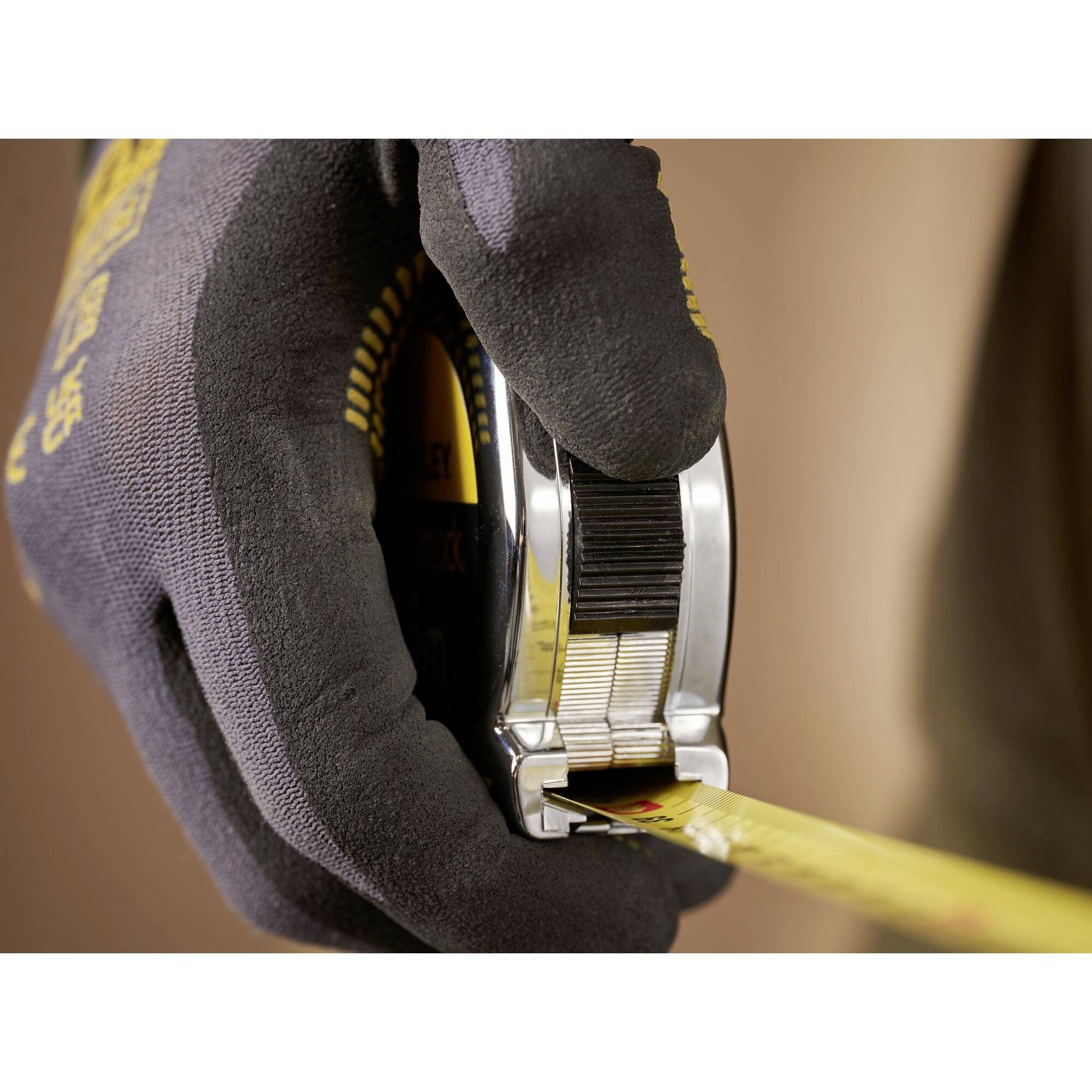 A hand wearing a glove is holding an unrolled tape measure. The scene suggests a measurement or construction work.