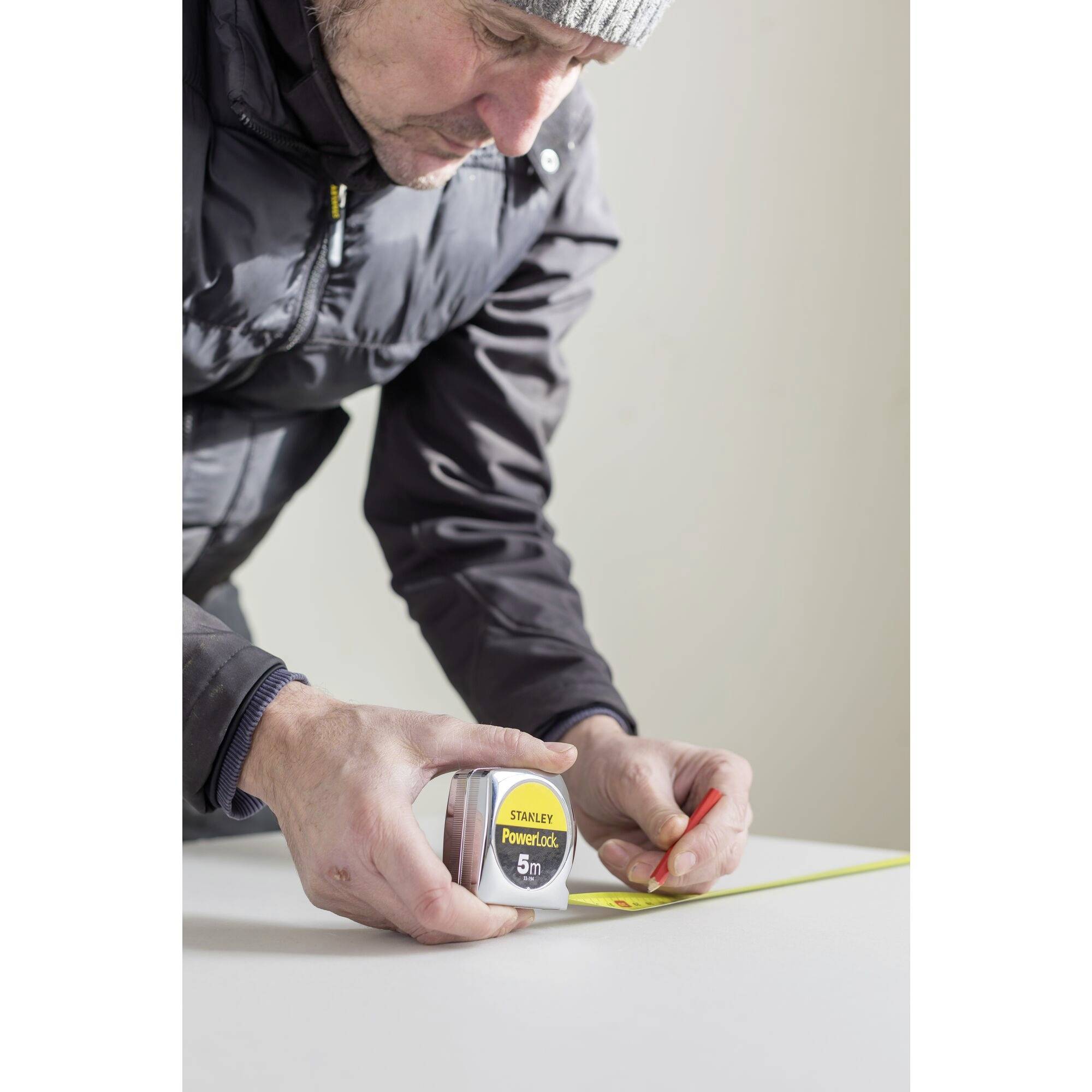 A person is measuring with a tape measure on a tabletop. The person is wearing a cap and winter clothing.