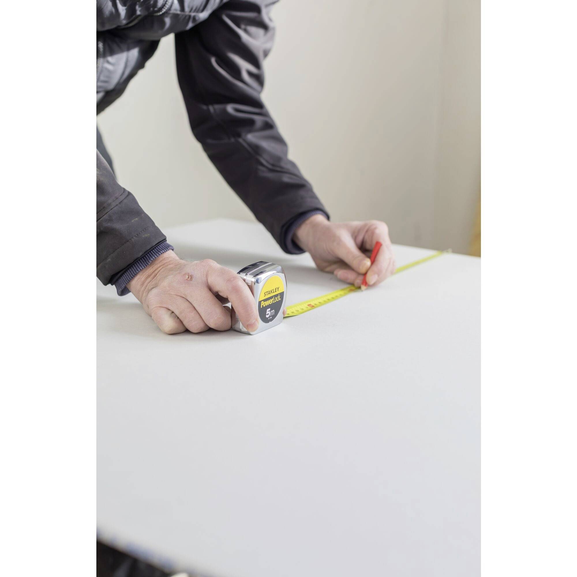 A person is measuring with a yellow tape measure on a white table.