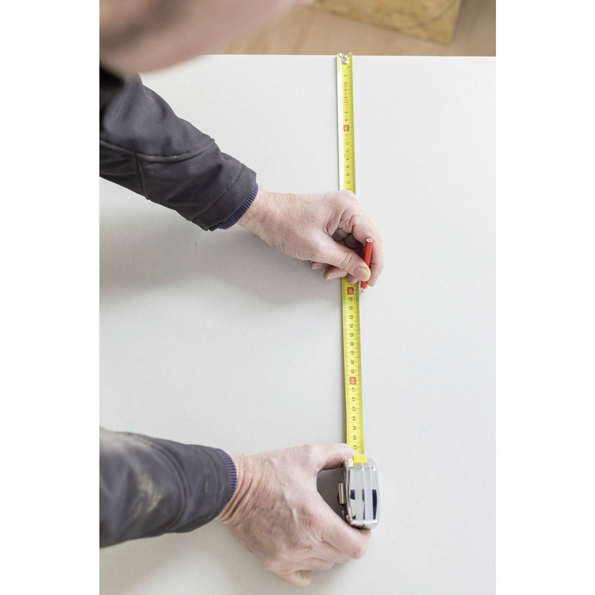 A person is measuring the length of a white surface with a yellow measuring tape.