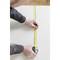 A person is measuring the length of a white surface with a yellow measuring tape.