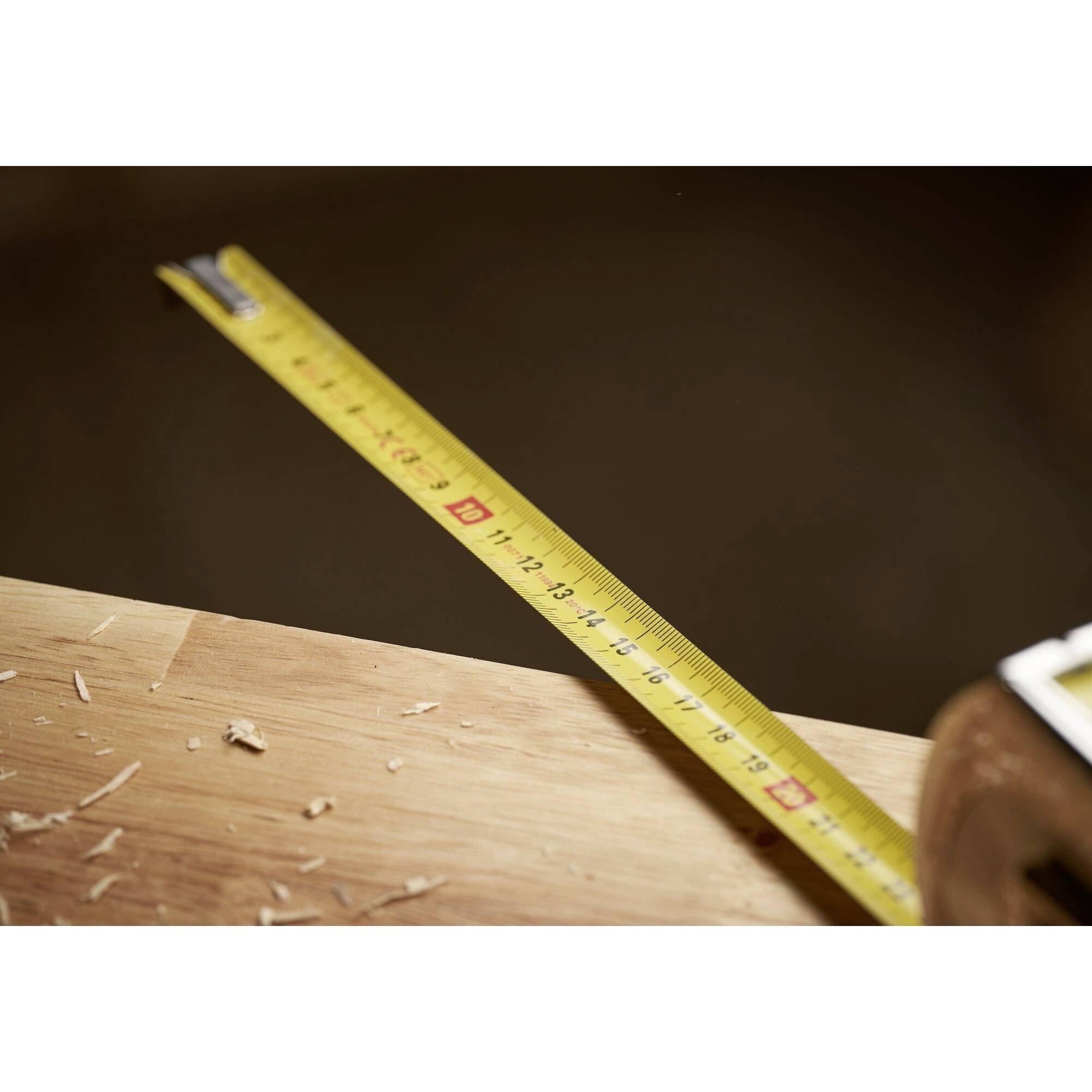A tape measure lies on a wooden table with wood shavings, showing the measuring of materials in a craftsman's workspace.