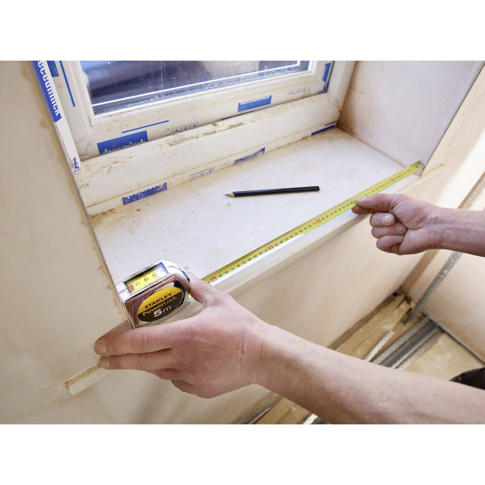 A window sill is being measured with a tape measure. One hand is holding the tape measure, while a pencil line is visible as a marking.