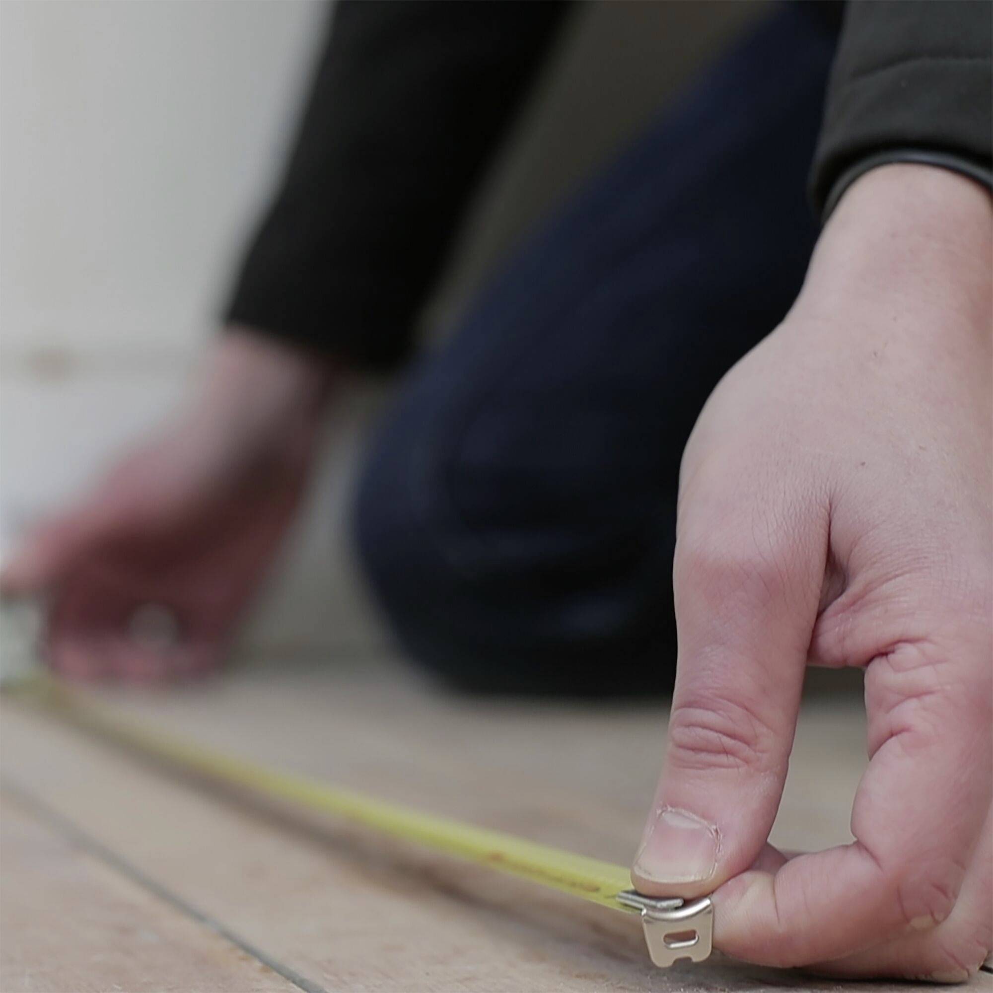 A person is measuring the floor with a tape measure positioned on a strip.
