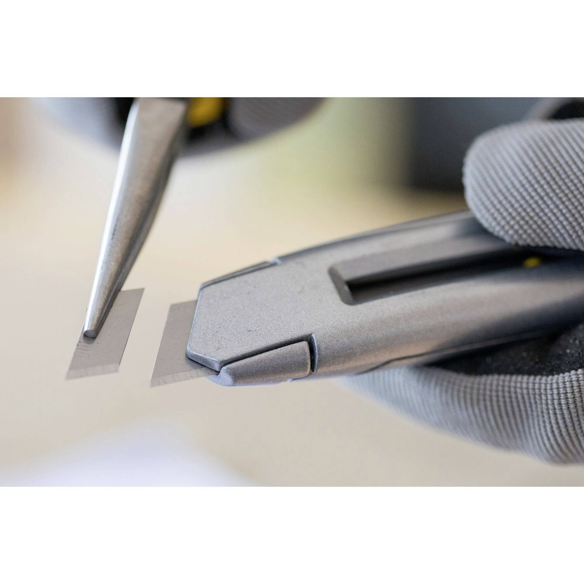 A close-up of hands wearing gloves working with tools shows precise cutting of a small rectangular material.