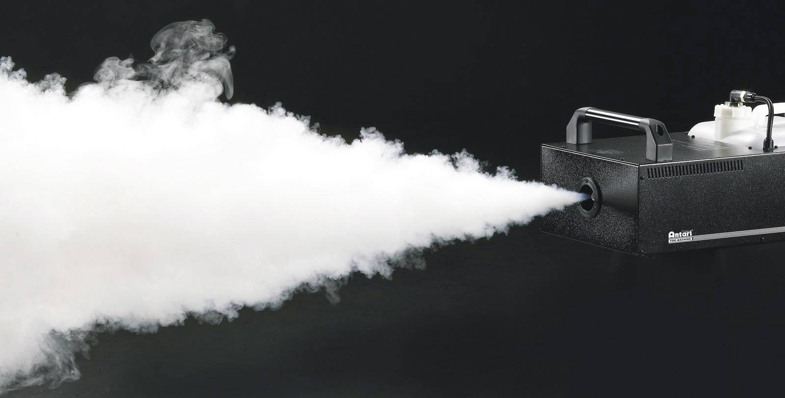 A fog machine generates a dense, white fog spray against a dark background.