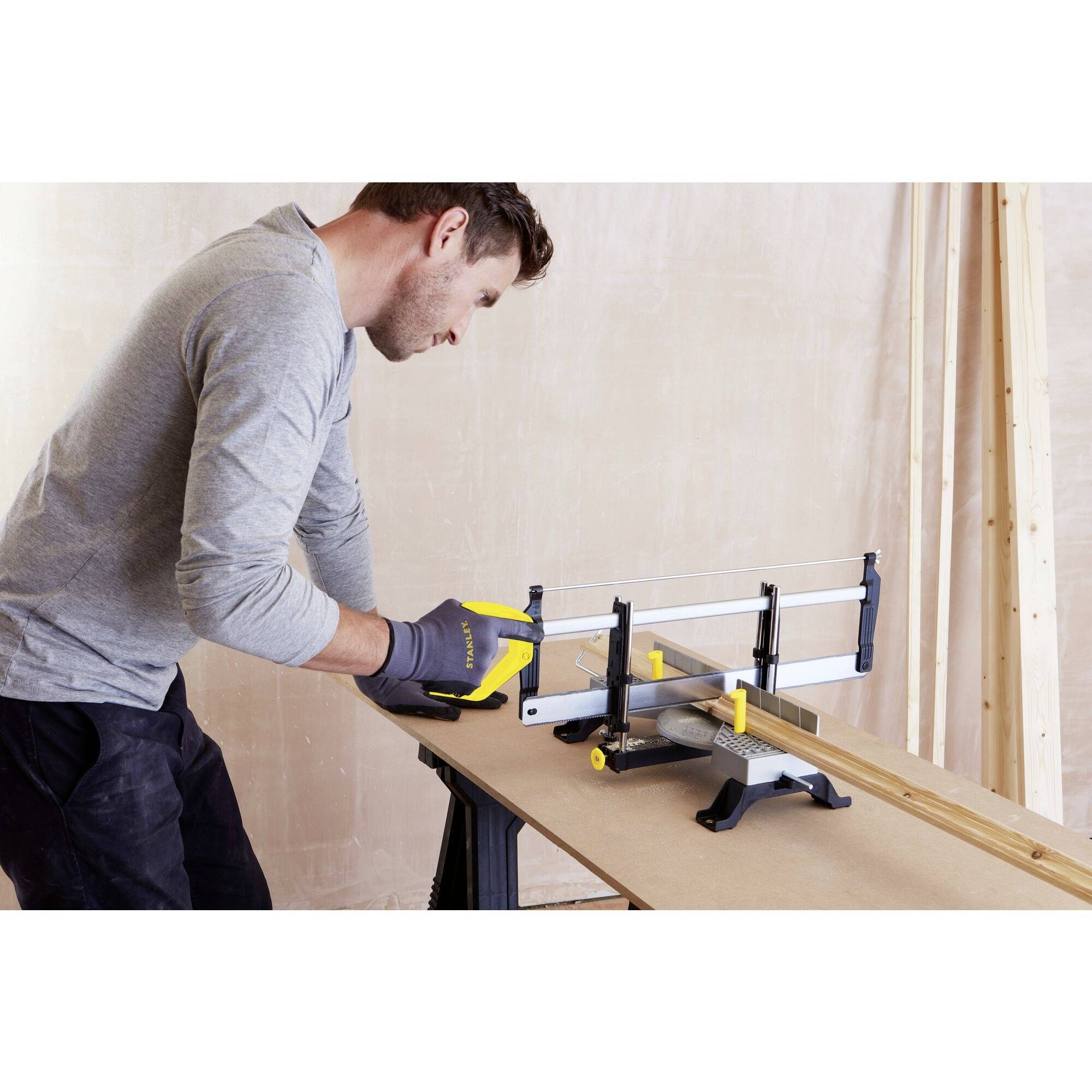 A man is using a handsaw with a sawing guide on a workbench for precise wood cutting. Focused on exact alignment and safety.