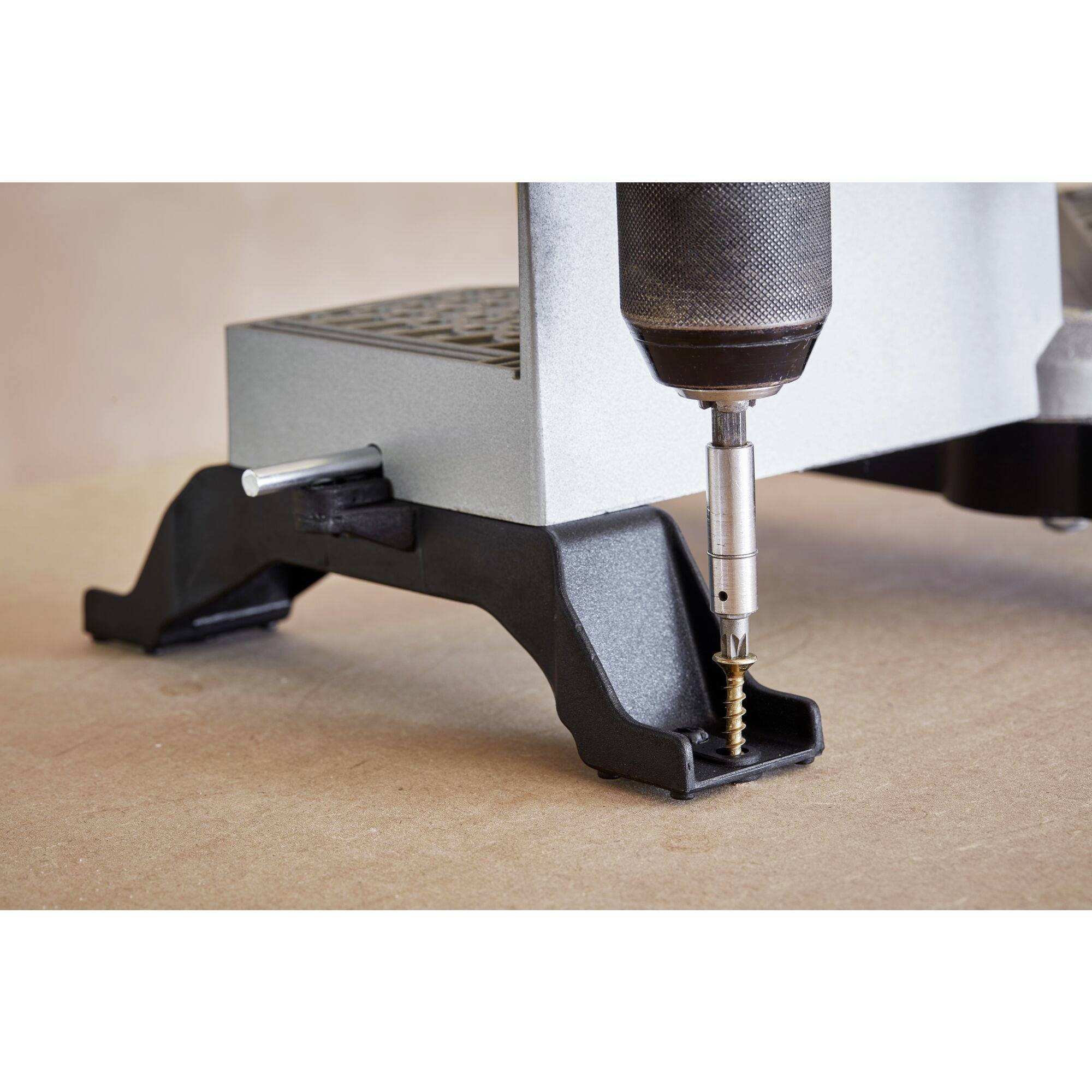 A cordless drill is screwing a golden screw into a wooden surface. The focus is on the tip of the drill and the screw.