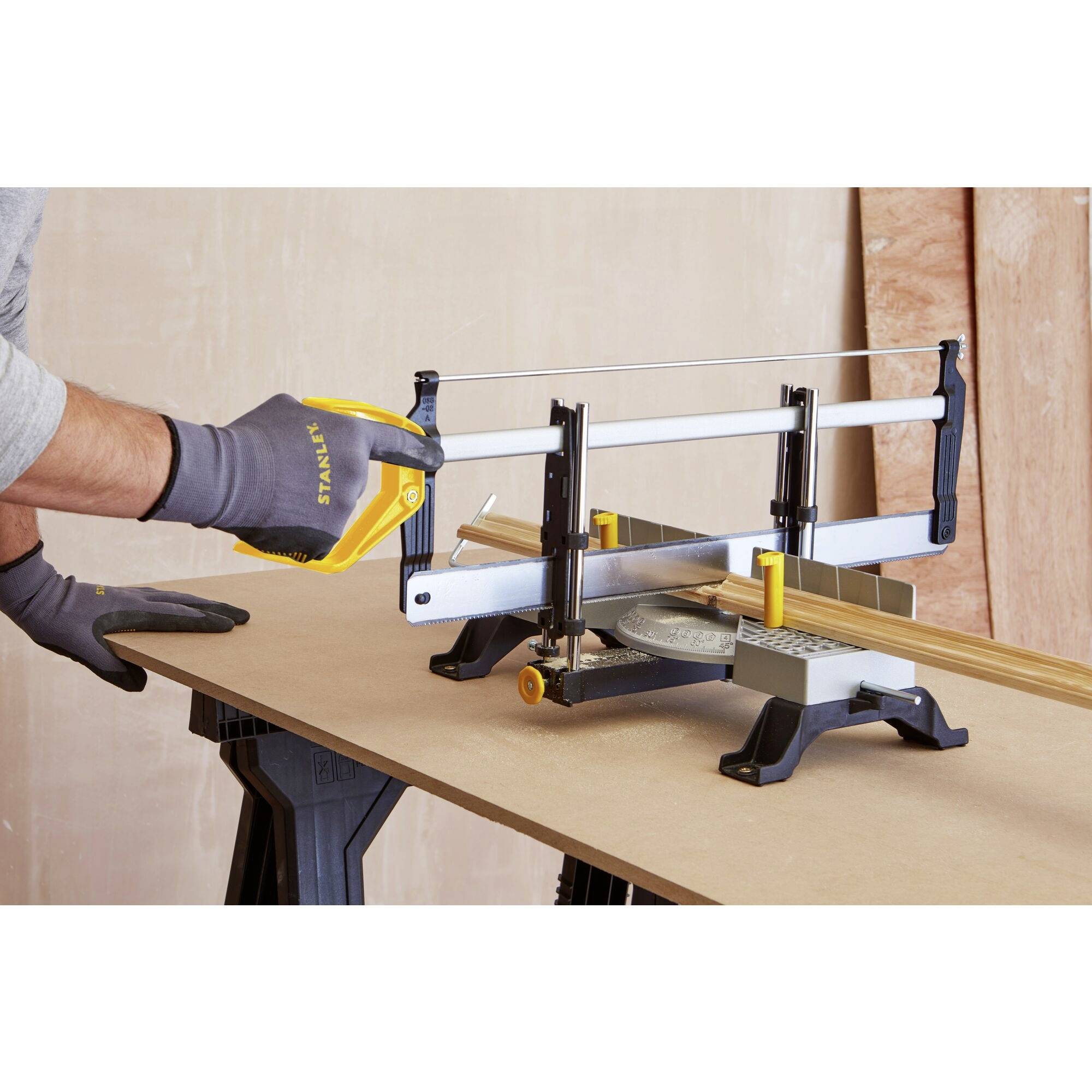 A person is sawing a piece of wood with a handsaw and mitre saw on a workbench. They are wearing work gloves.