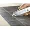 A hand holds a silver-coloured utility knife with the inscription 'Stanley 99E', cutting precisely through a black tile surface.