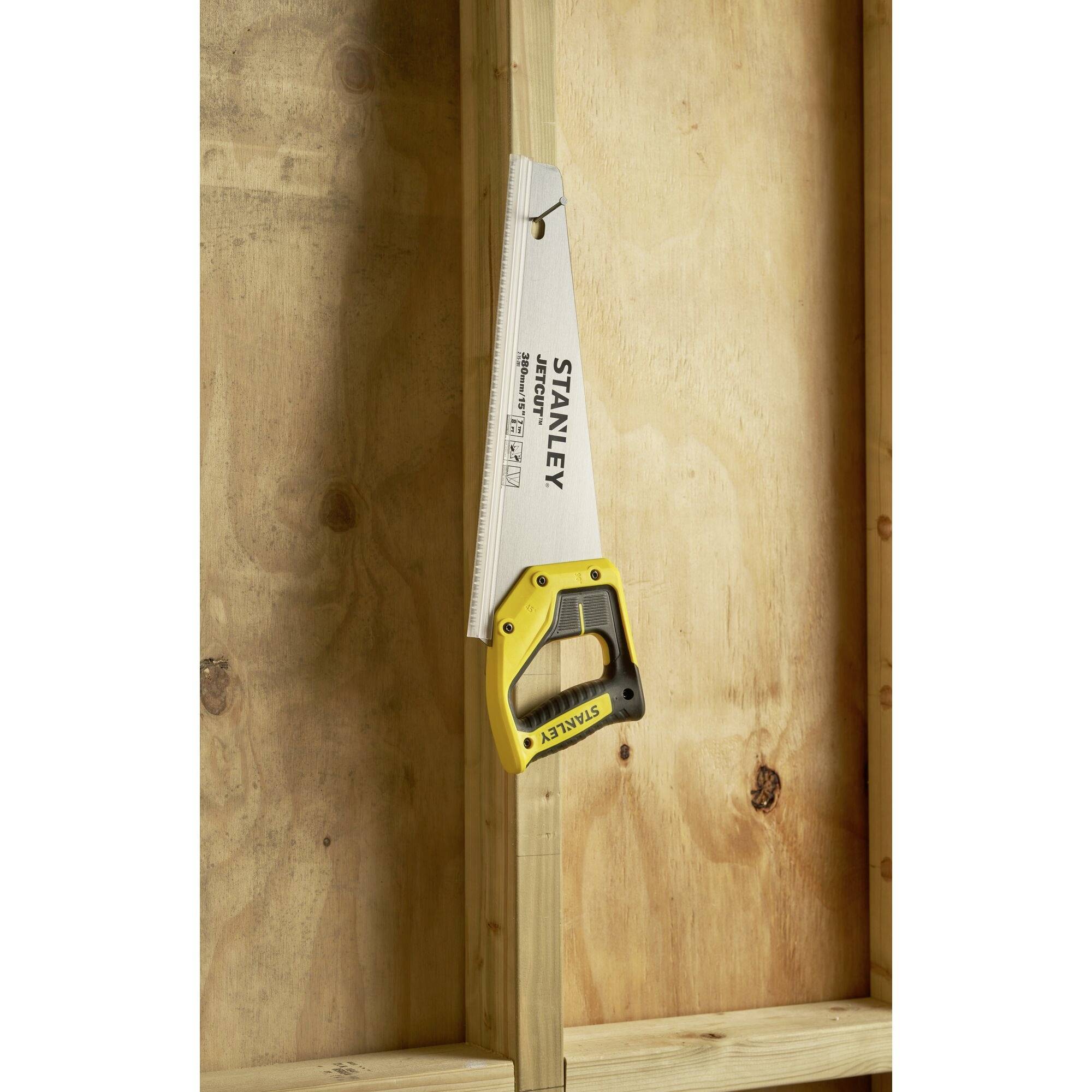 A hand saw with a yellow handle is placed in a wooden frame. It is positioned vertically, with the blade pointing upwards.