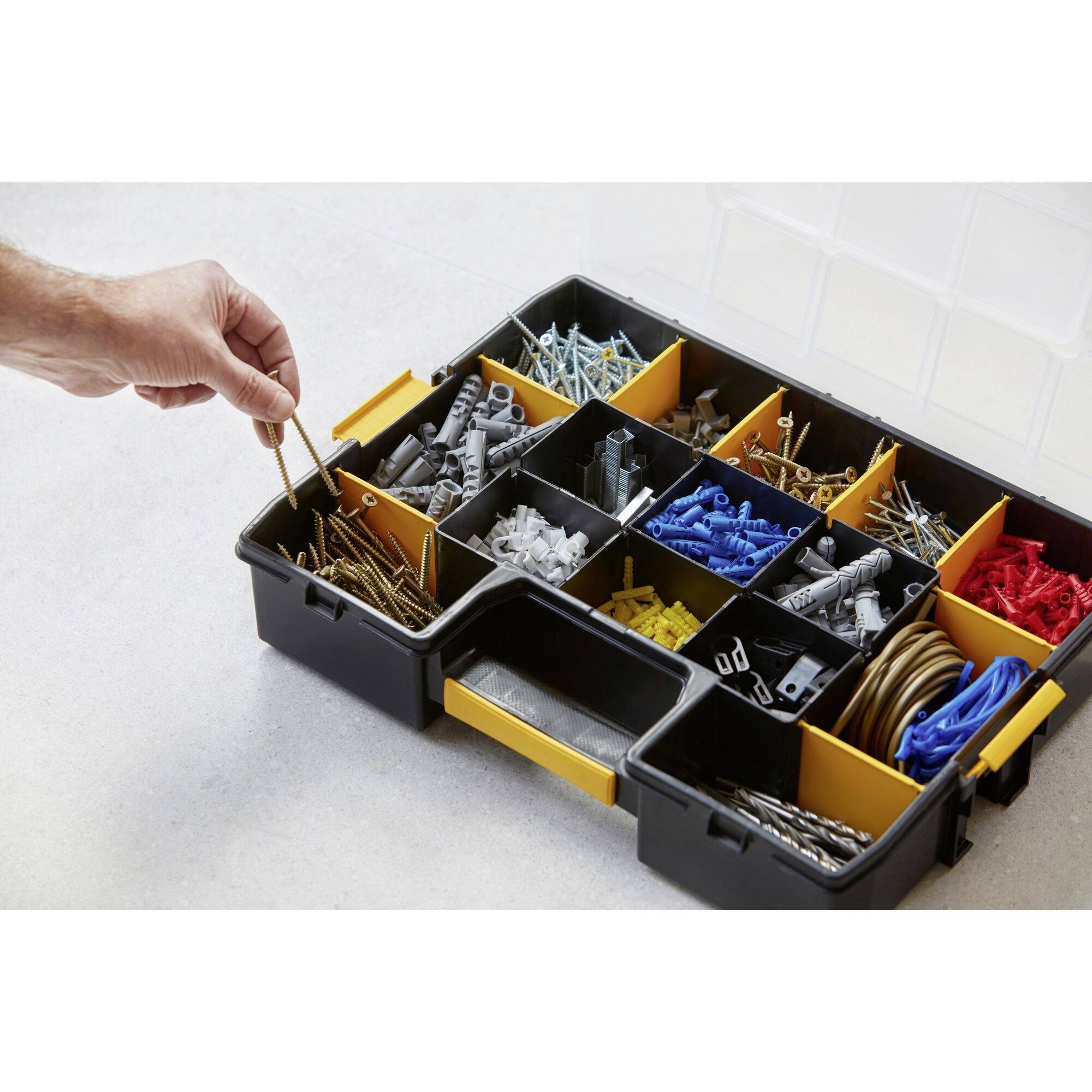 A hand takes a screw from an open organiser with various compartments containing different screws, bolts and wall plugs.
