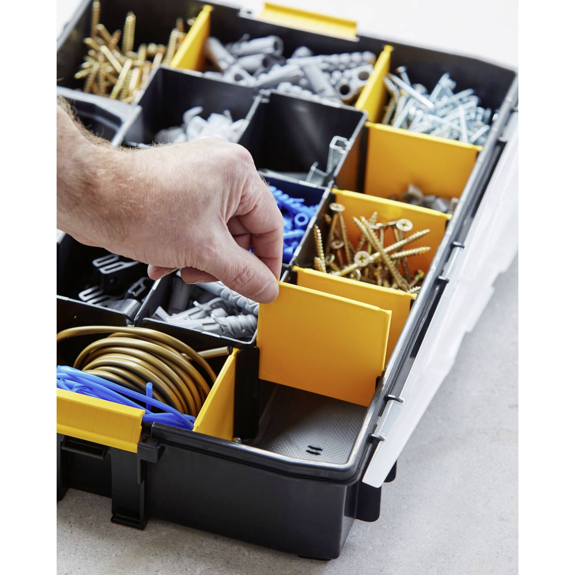 An open toolbox with multiple compartments containing various screws, wall plugs, and cable types. A hand reaches for a screw.