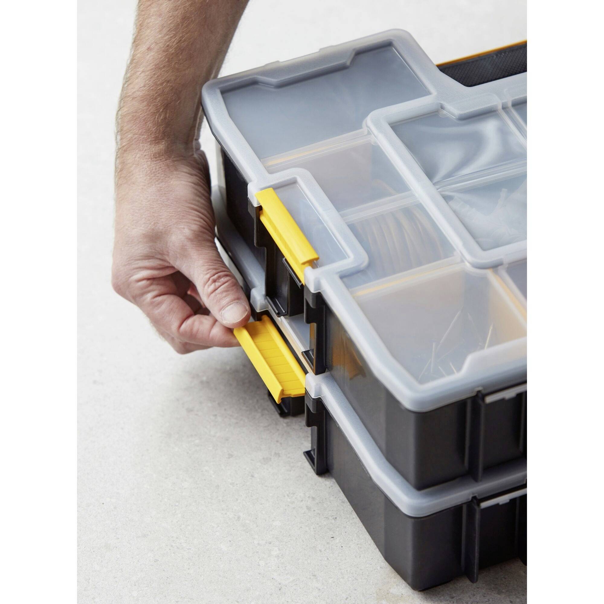 A hand opens a black toolbox with yellow latches. The box contains various compartments for tools.