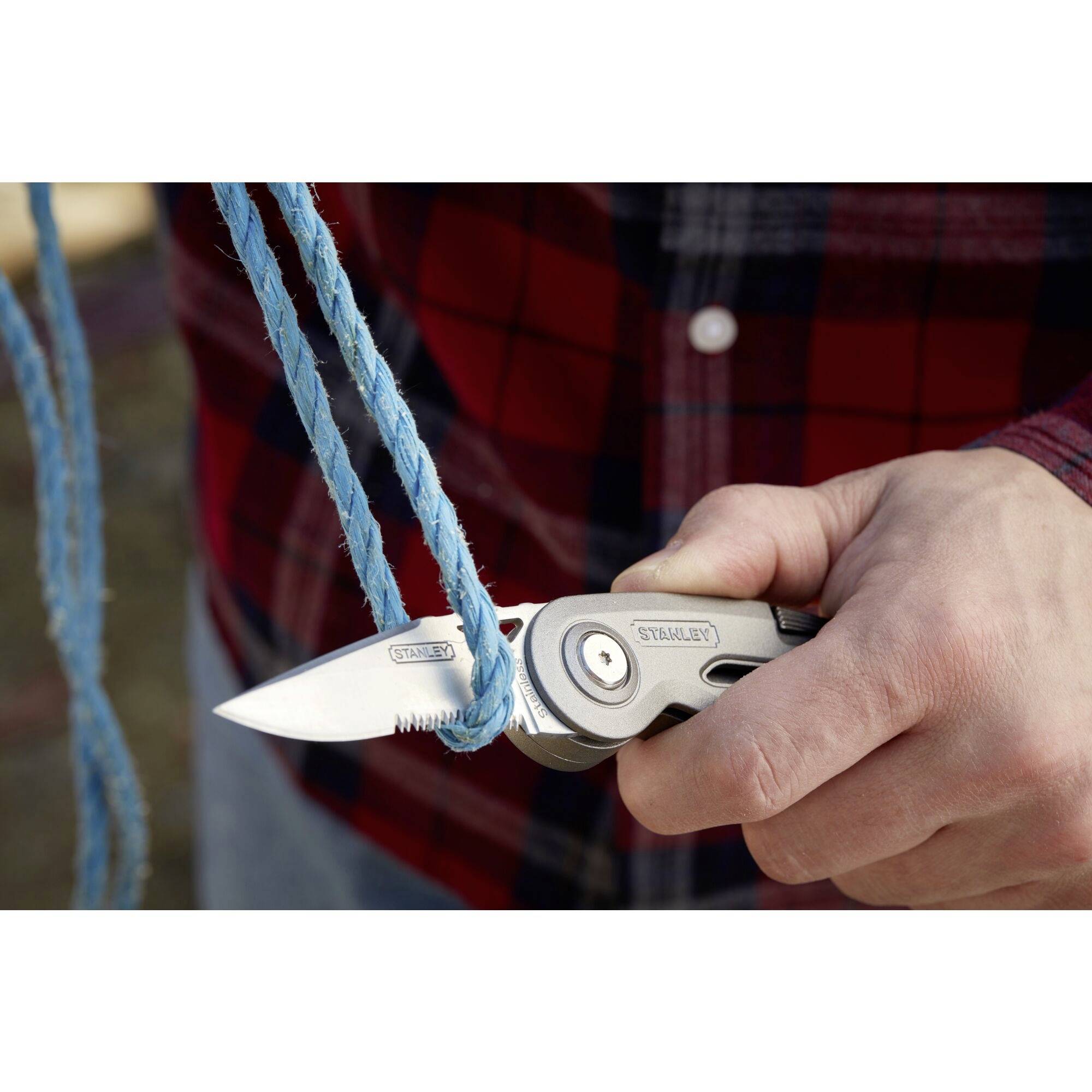 'Close-up of a hand cutting a blue rope loop with a penknife; person wearing a red checked shirt.'
