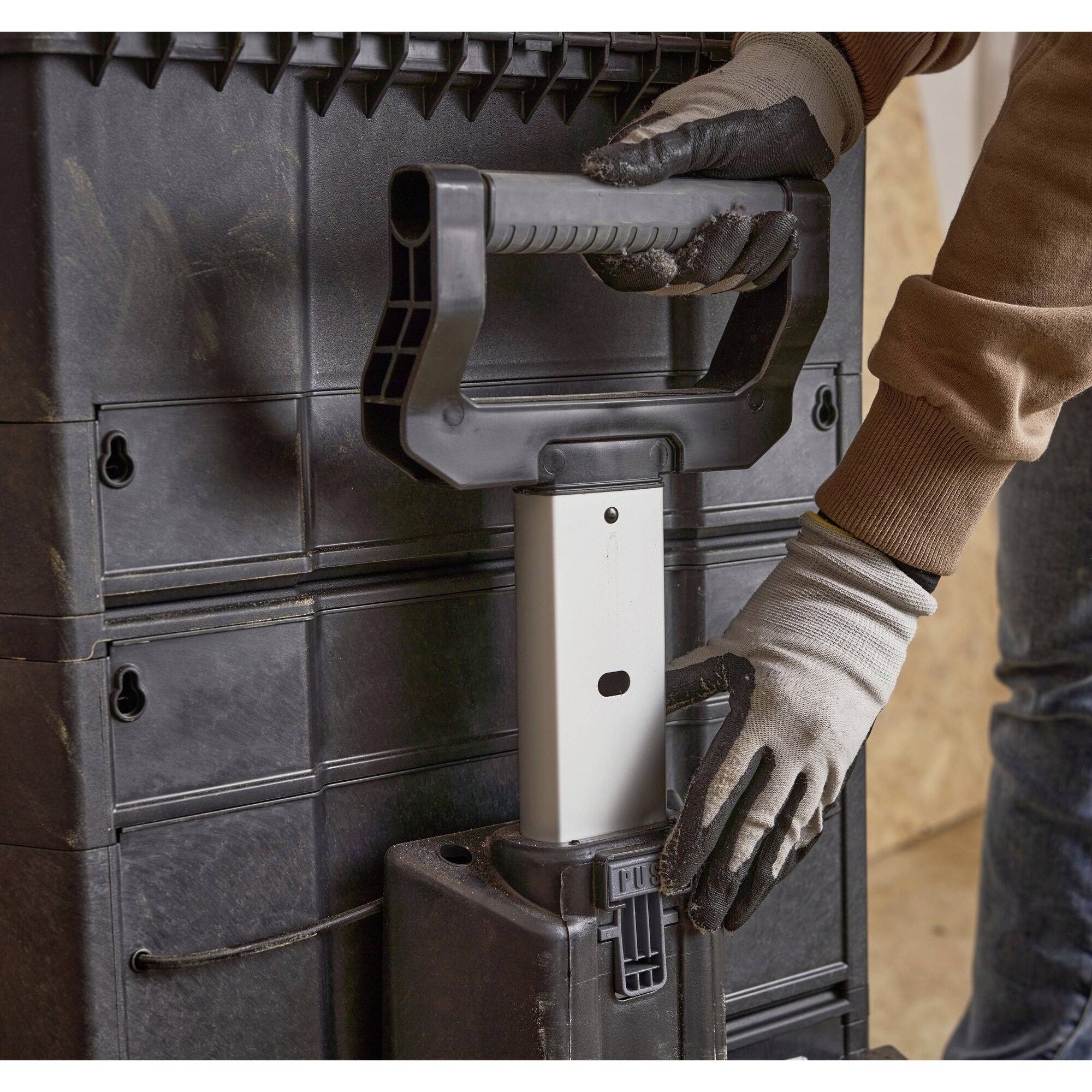 A person wearing work gloves pulls on a handle attached to a case. The background shows a dark wall.