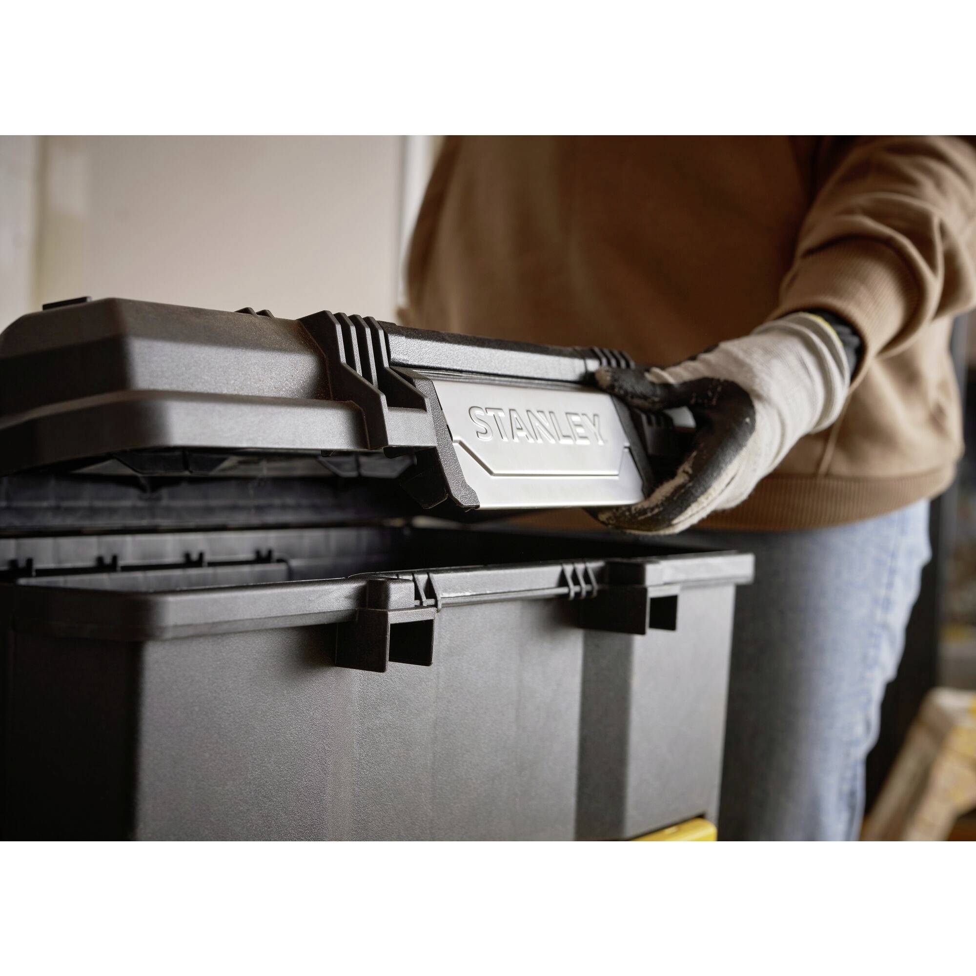 A person opens a black toolbox. The box has a handle with the embossed inscription 'STANLEY'.
