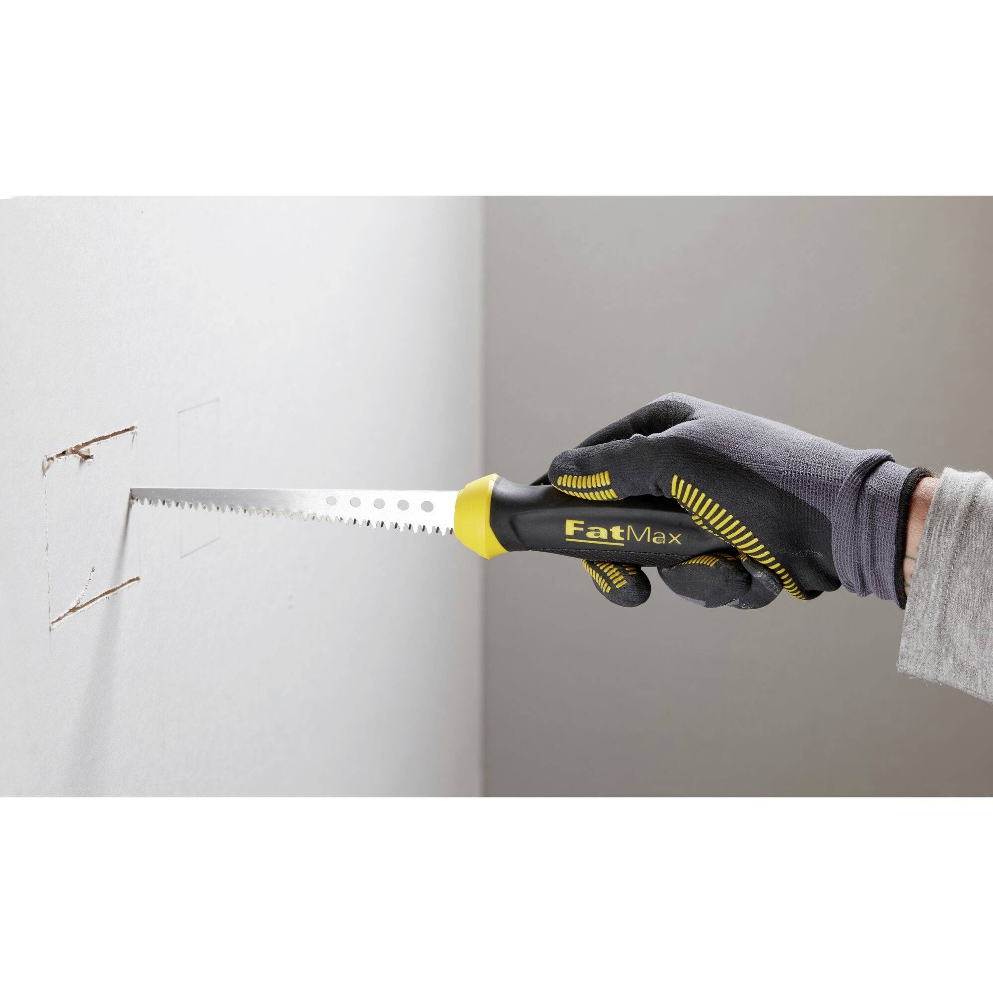 A person is cutting a rectangle into a plasterboard wall using a handsaw. They are wearing a glove and gripping the tool firmly.