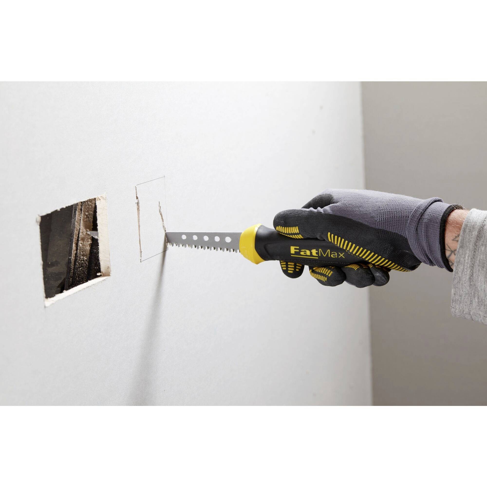 A person is cutting a square hole in a plasterboard wall using a handsaw.