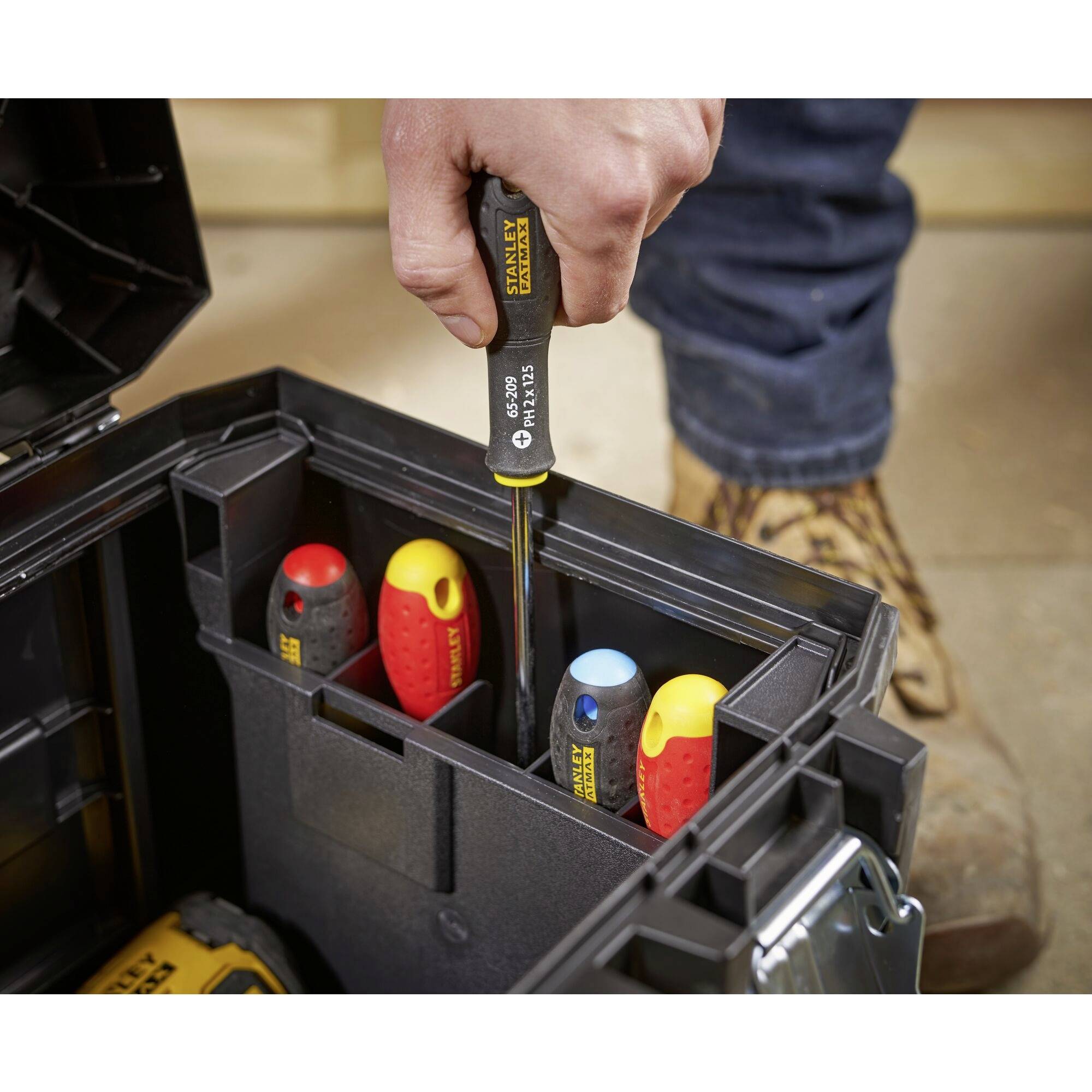 A toolbox with an open drawer displays various screwdrivers. A person is holding a screwdriver.